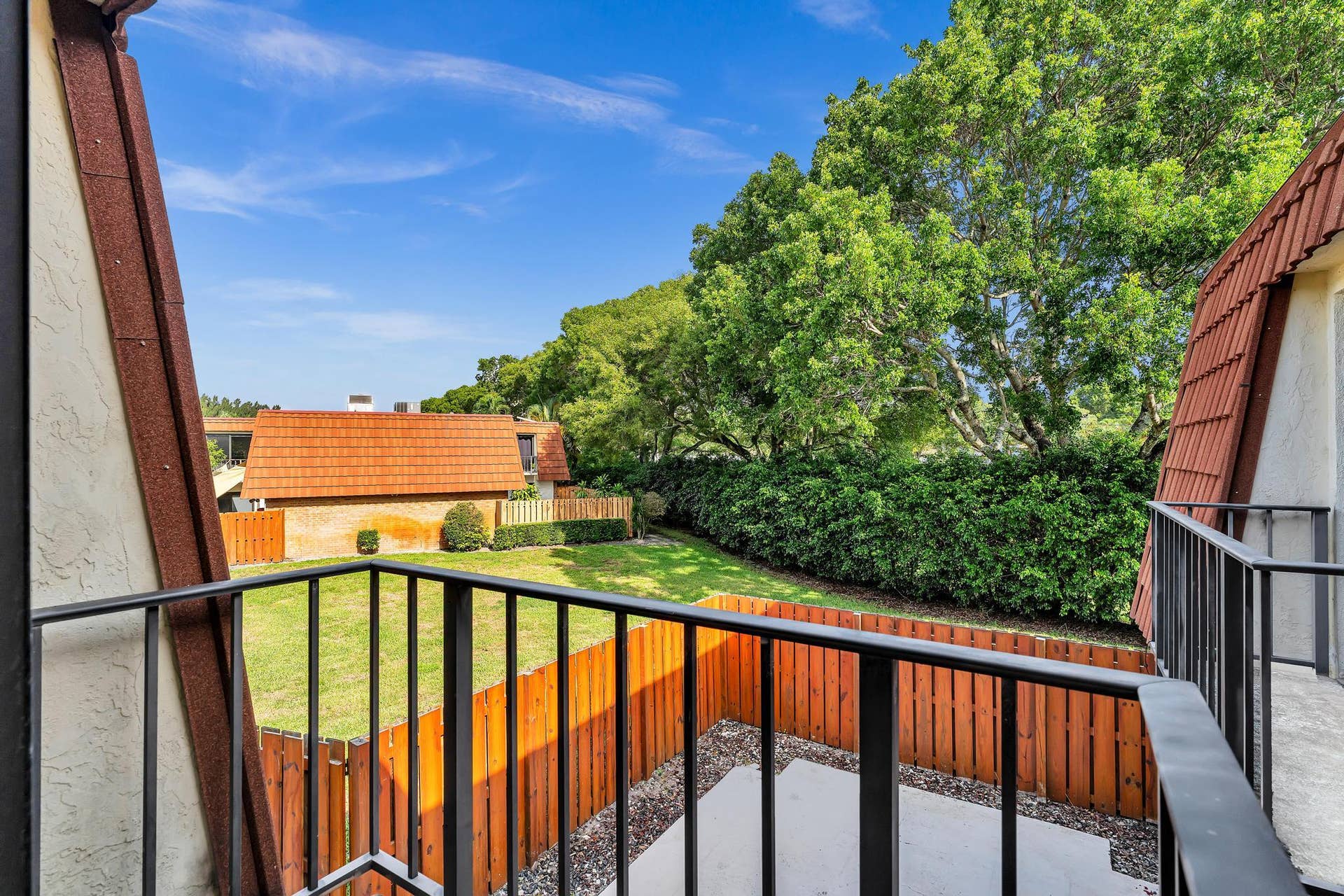 Balcony with black metal railings, overlooking a private fenced yard with a concrete patio