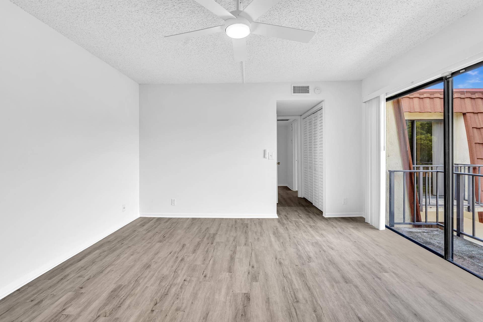 Spacious room featuring wood-finish flooring, white walls, and a ceiling fan with integrated lighting