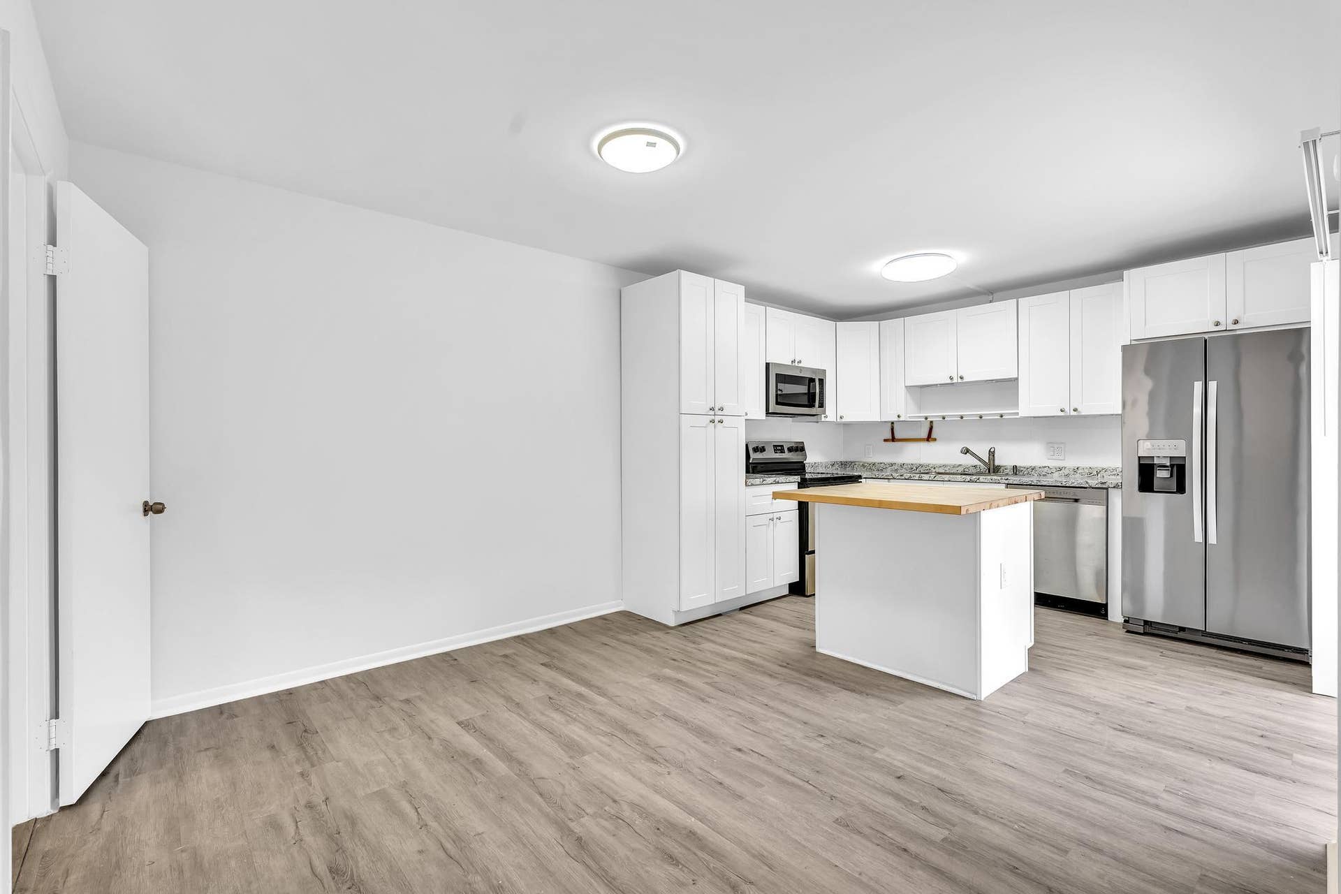 Open-concept kitchen featuring white cabinetry, gray speckled countertops, stainless steel appliances, a center island with a wood-finish top, and wood-finish flooring