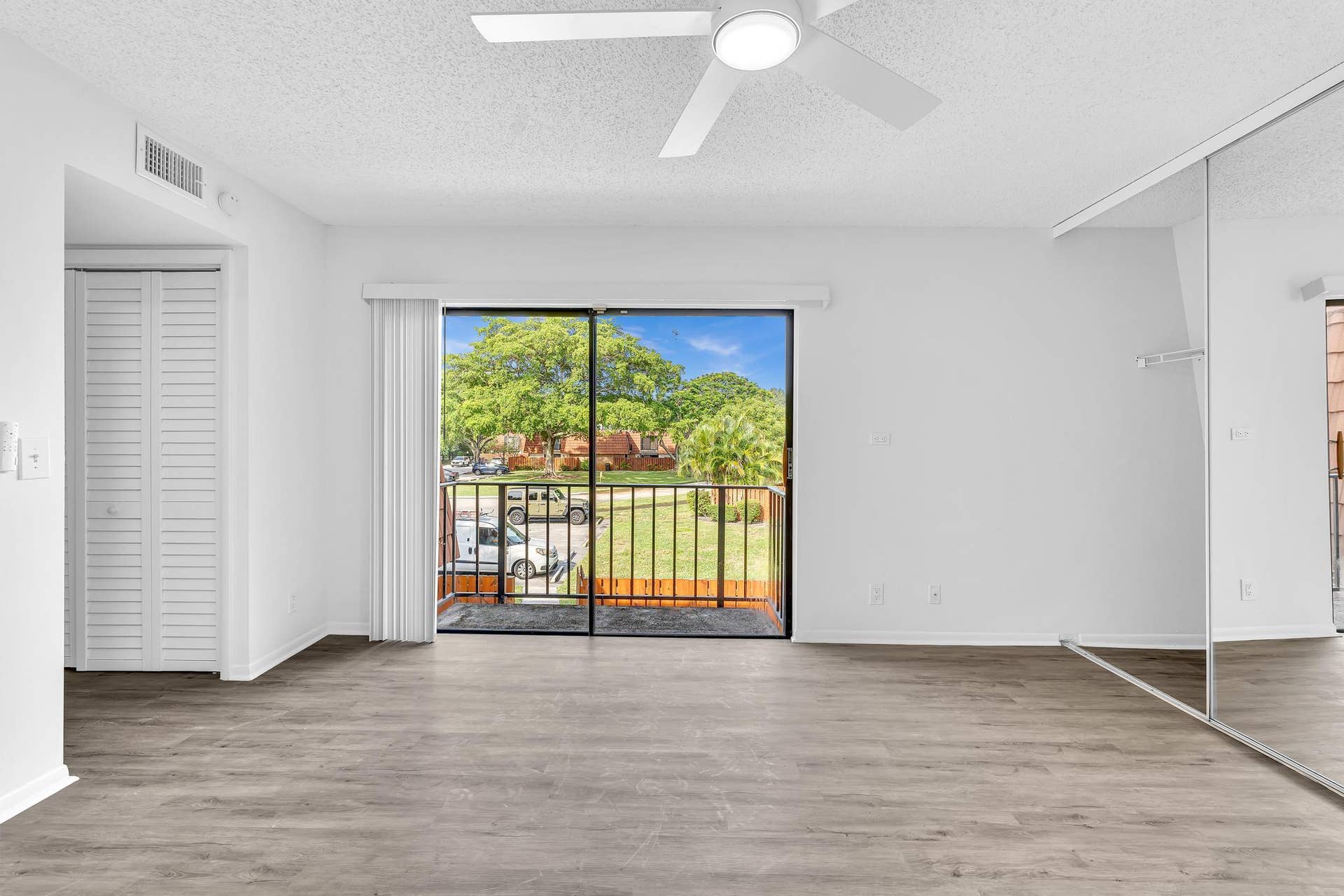 Open room featuring wood-finish flooring, a ceiling fan with integrated lighting, mirrored closet doors, and a sliding glass door to a private balcony