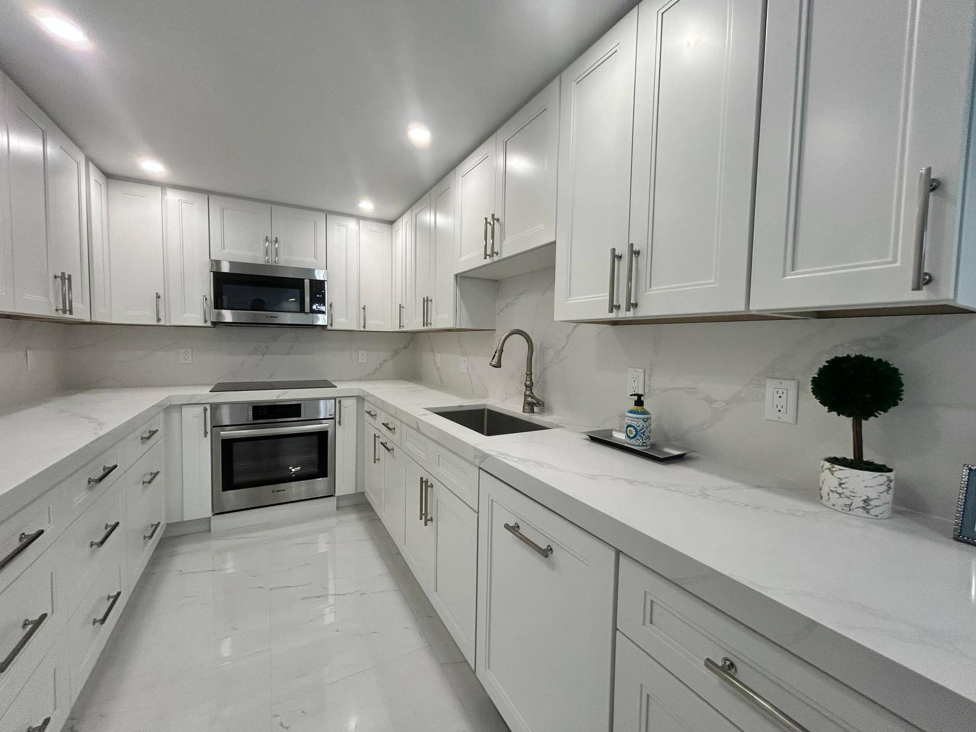 U-shaped kitchen featuring white shaker cabinetry, stainless steel appliances, white countertops, and a complementary backsplash
