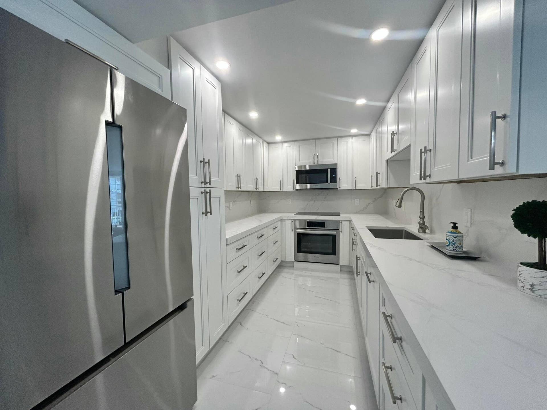 Contemporary kitchen featuring white cabinetry, stone countertops, stainless steel appliances, and integrated lighting