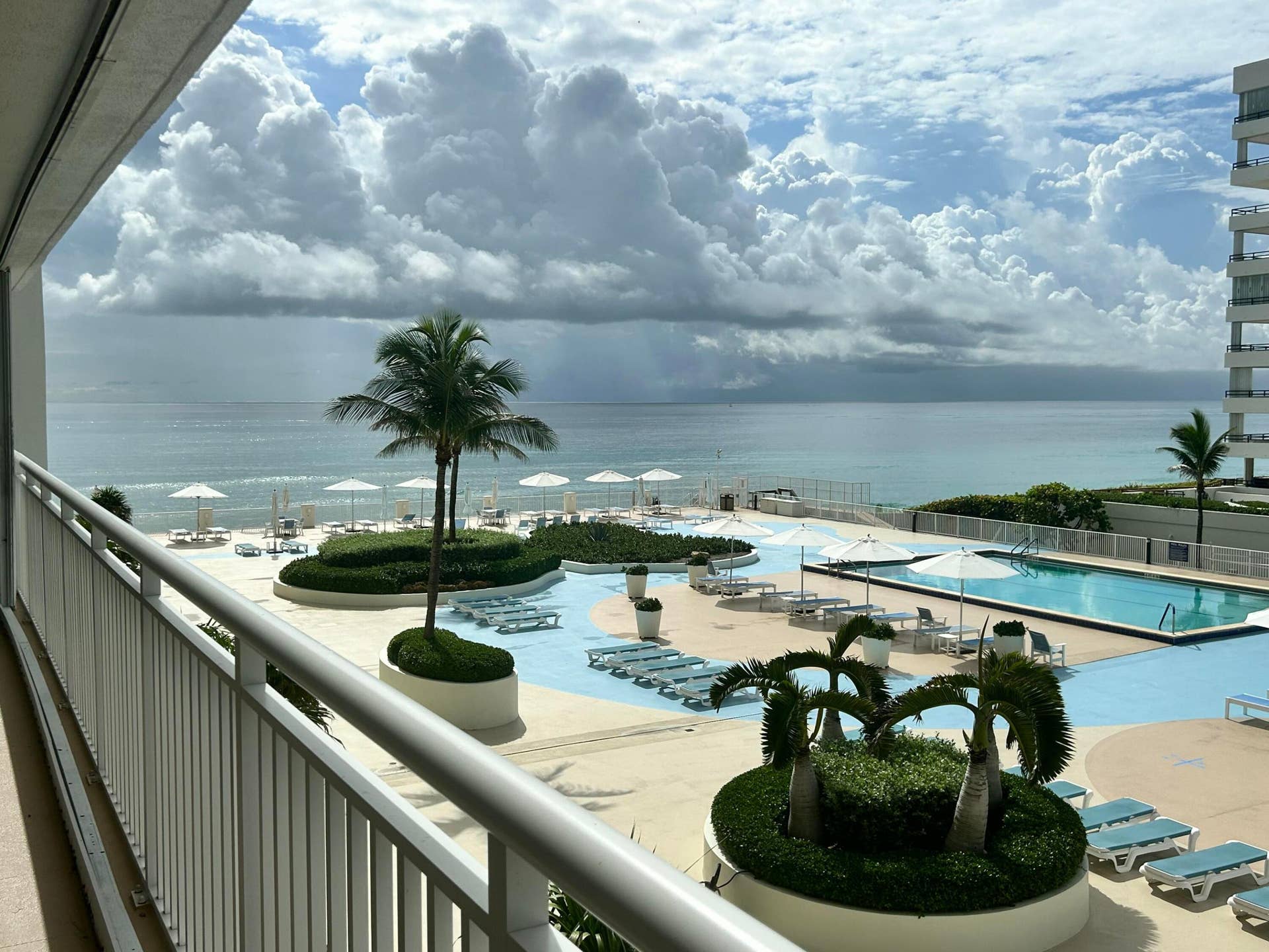 Expansive outdoor living area featuring a resort-style pool deck, multiple swimming pools, manicured landscaping with palm trees, and direct beach access