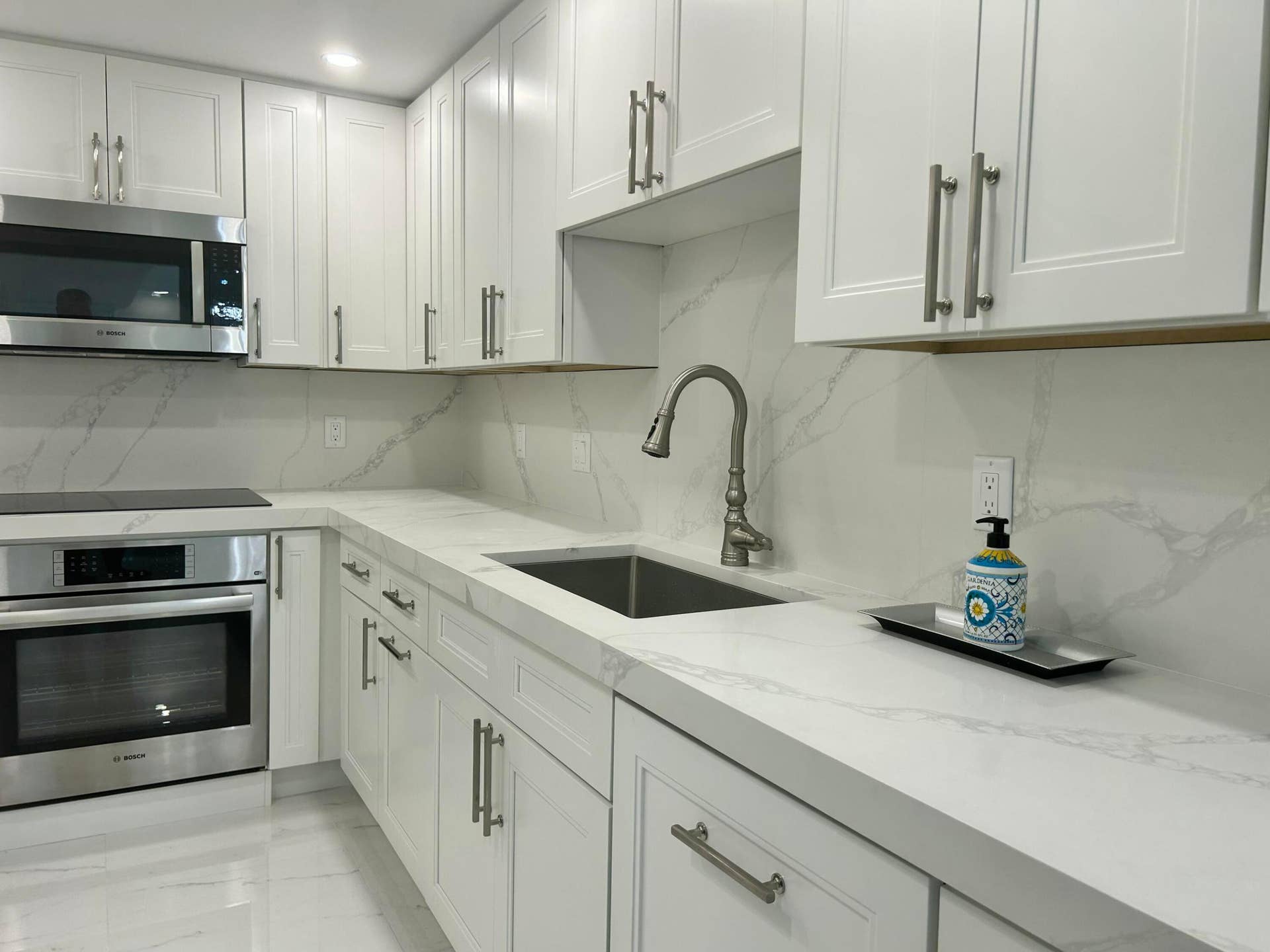 Modern kitchen featuring white shaker cabinetry with brushed nickel hardware, light-toned countertops, and a matching full-height backsplash