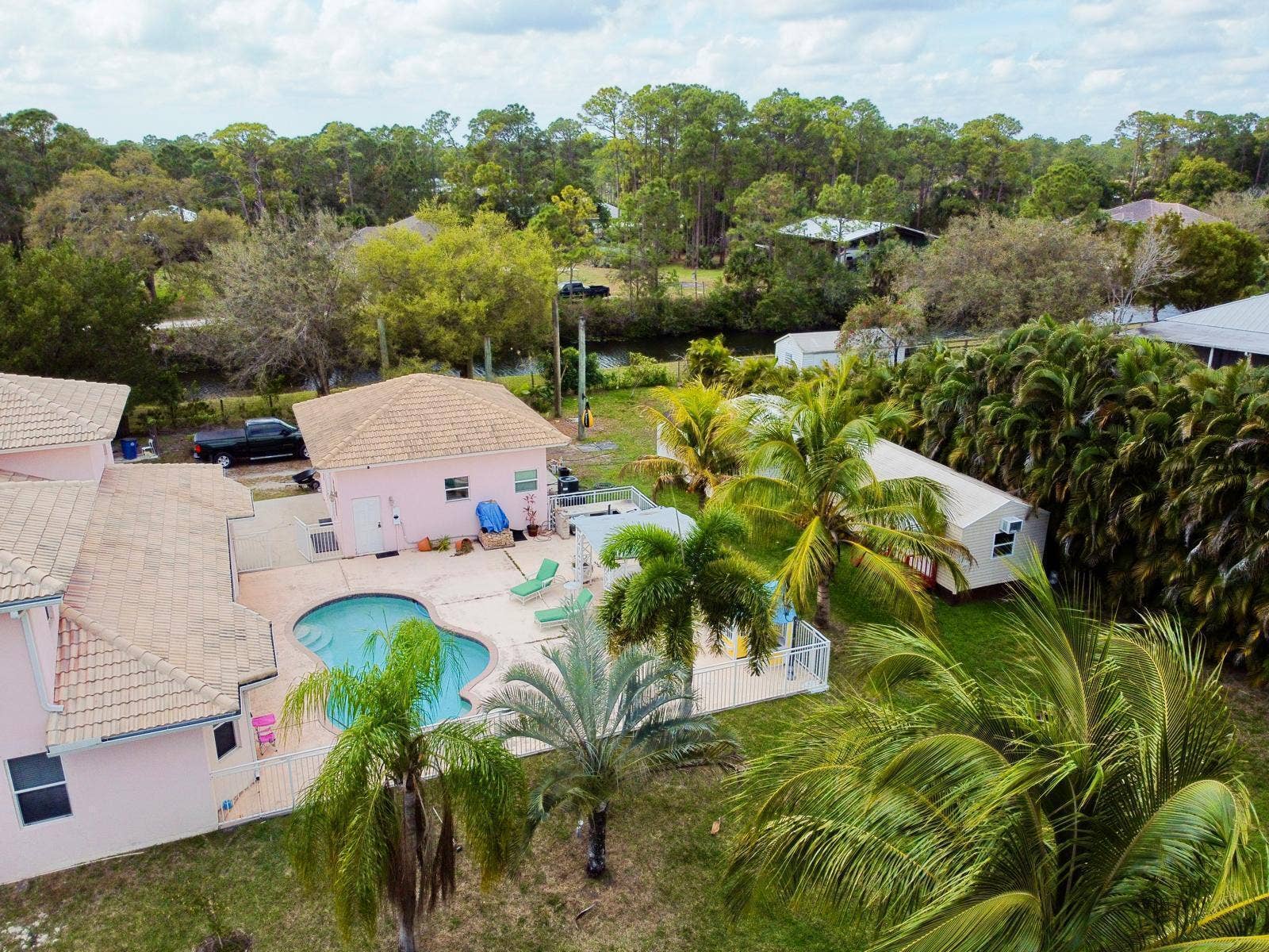 Property featuring a kidney-shaped pool, extensive hardscaping, a detached auxiliary structure, and established tropical landscaping