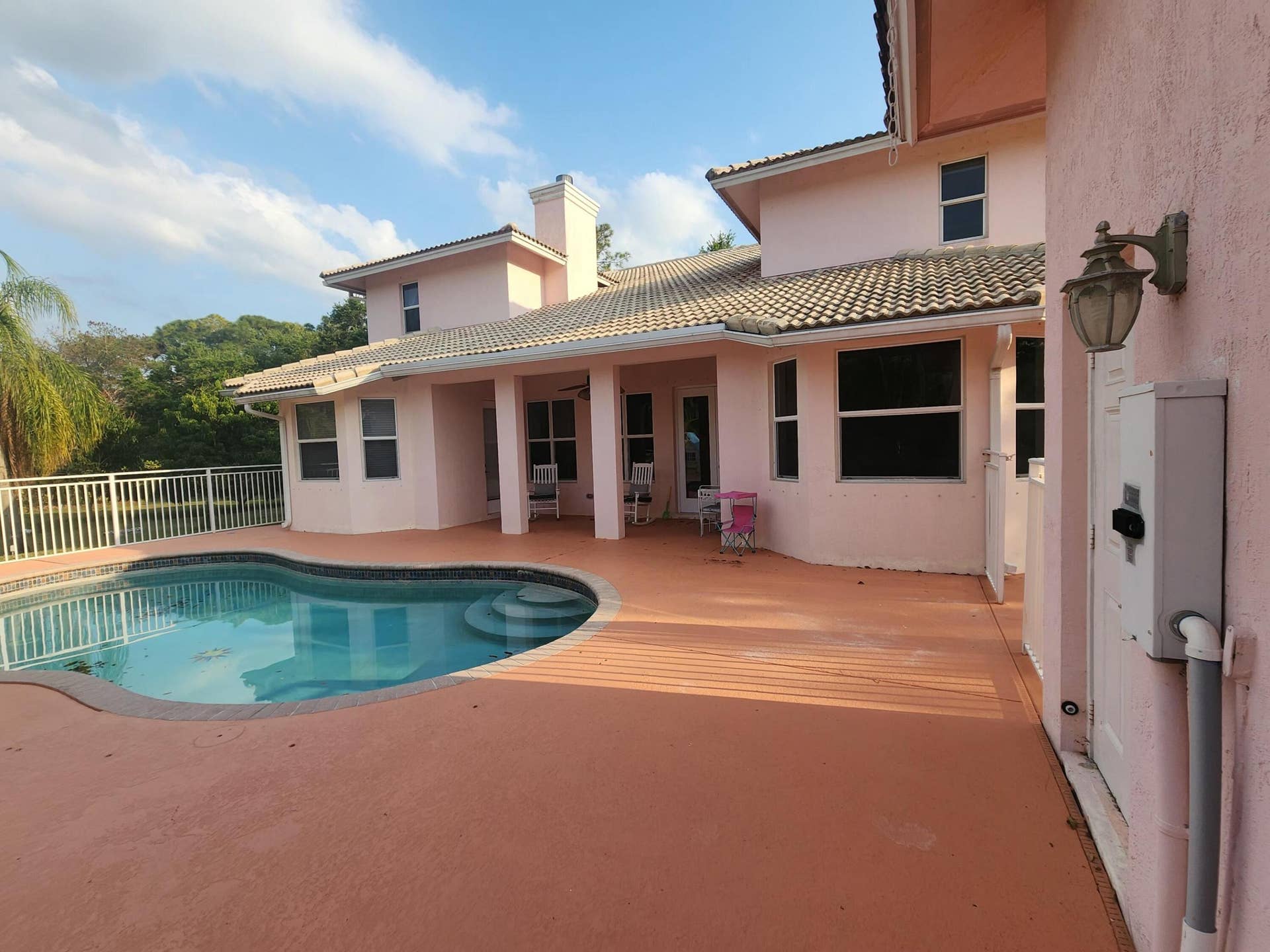 Resort-style backyard featuring a freeform swimming pool with steps, a spacious paved deck, and a covered patio