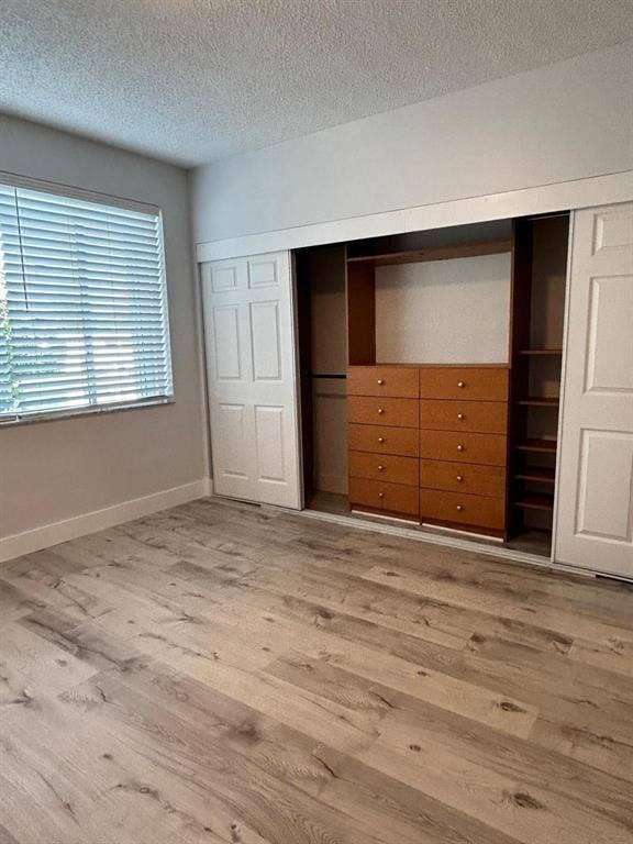 Room featuring light wood-finish flooring, a window with horizontal blinds, and a built-in closet system with sliding bifold doors and integrated drawers