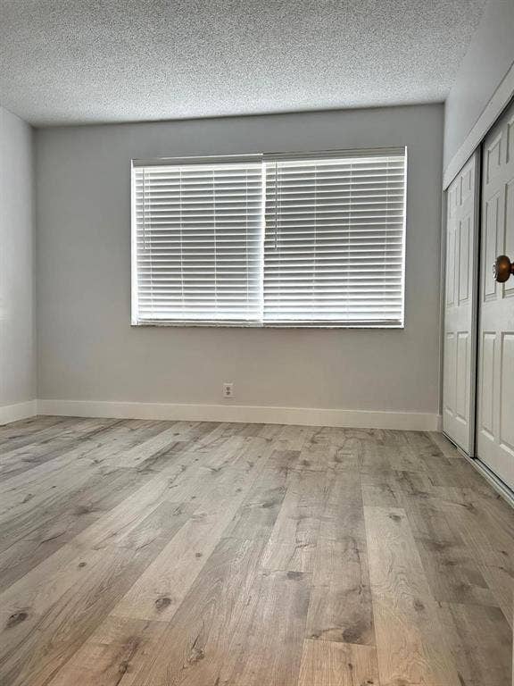 Light-toned wood-finish flooring complements the neutral wall color in this room featuring a window with blinds and white baseboards