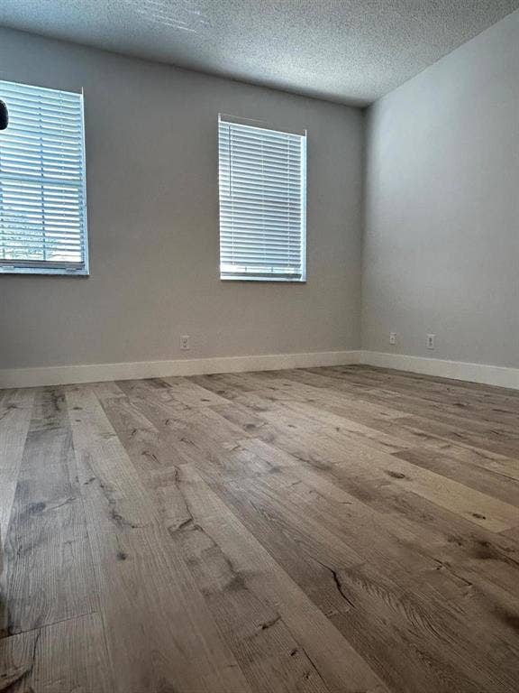 Spacious room featuring wood-finish flooring, neutral wall tones, white baseboards, and two windows with blinds