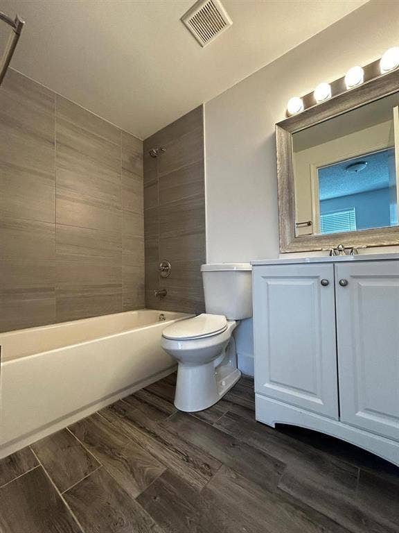 Full bathroom featuring wood-finish tile flooring, a white vanity with cabinet storage, a framed vanity mirror with overhead lighting, a white toilet, and a bathtub with gray subway tile surround