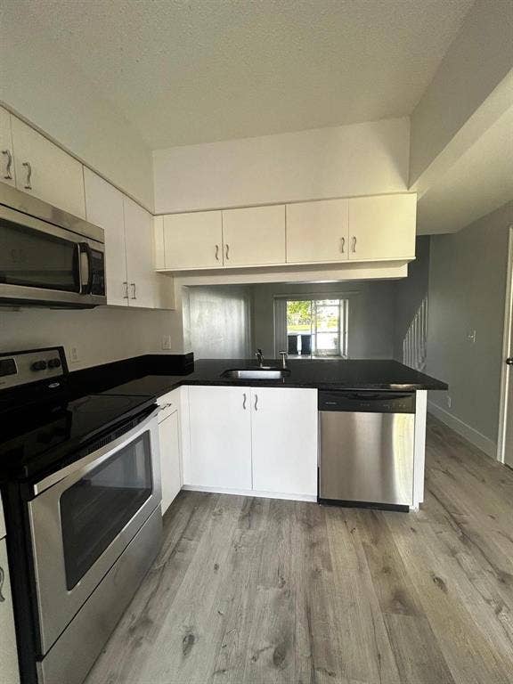 Kitchen featuring white cabinetry, stainless steel appliances, dark countertops, and wood-finish flooring
