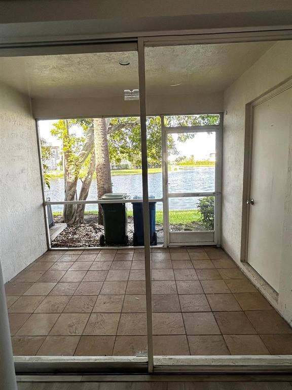 Screened patio featuring earth-toned tile flooring, direct water access, and mature trees