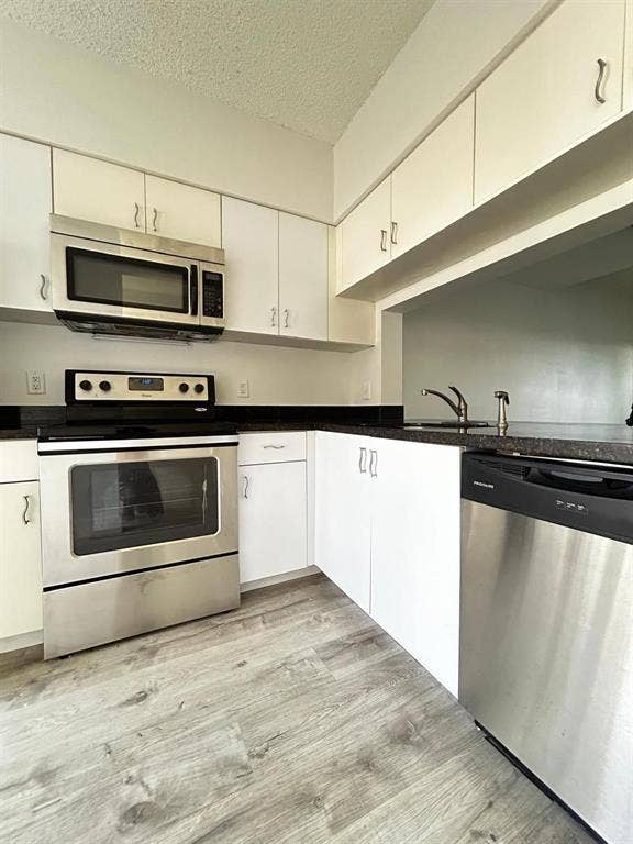 Kitchen featuring white cabinetry, dark countertops, and wood-finish flooring