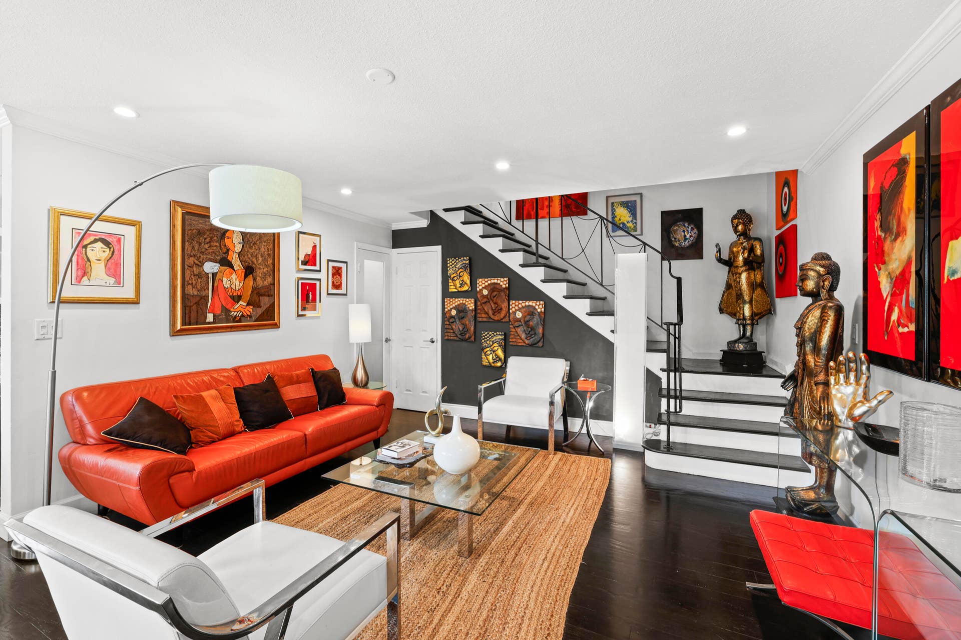 7 Middlesex Drive, Wilton Manors, FL 33305 Modern living space showcasing a vibrant red curved sofa, wood-finish flooring, and dramatic architectural elements including a floating staircase with metal railings
