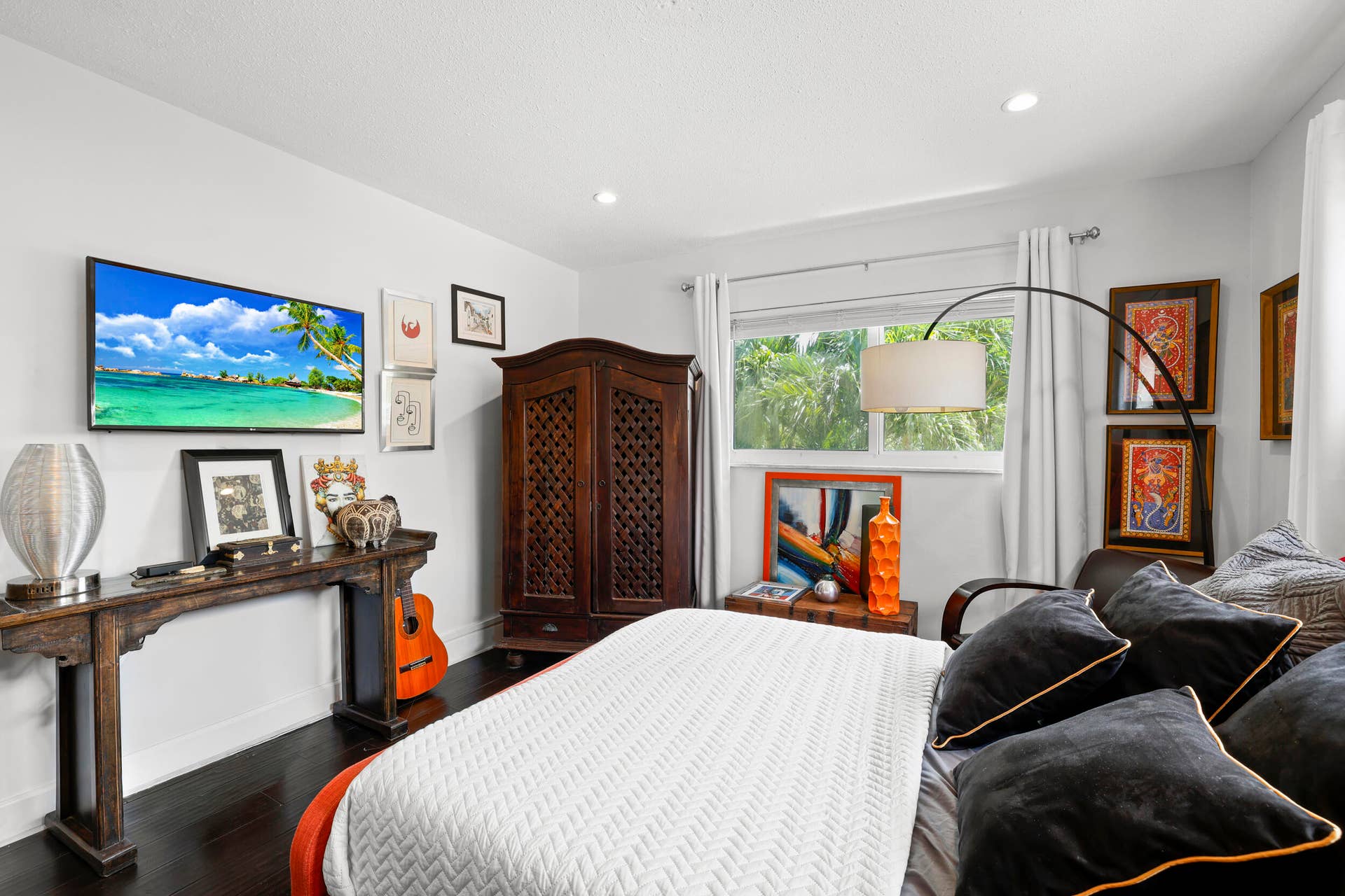 7 Middlesex Drive, Wilton Manors, FL 33305 Sophisticated primary bedroom showcasing dark wood-finish flooring, a custom wood wardrobe with decorative lattice detailing, and crisp white bedding accented with black and gold pillows