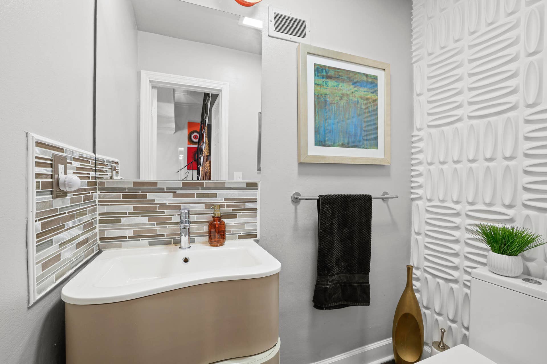 7 Middlesex Drive, Wilton Manors, FL 33305 Modern bathroom featuring a curved vanity with integrated sink, striped tile backsplash in neutral and metallic tones, and chrome fixtures