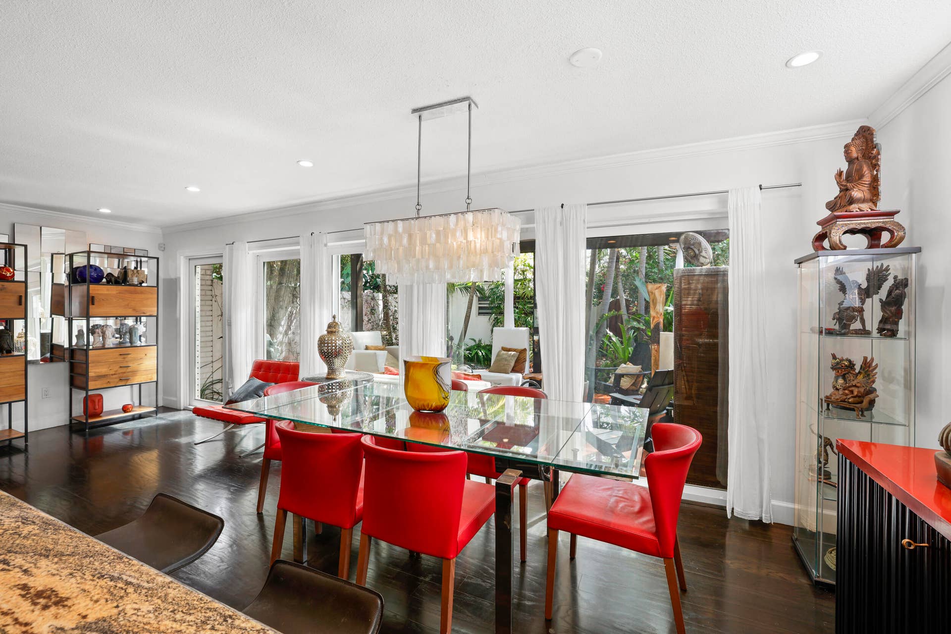 7 Middlesex Drive, Wilton Manors, FL 33305 Sophisticated dining space featuring a glass-top table, red upholstered chairs, and abundant natural light from expansive glass doors and windows