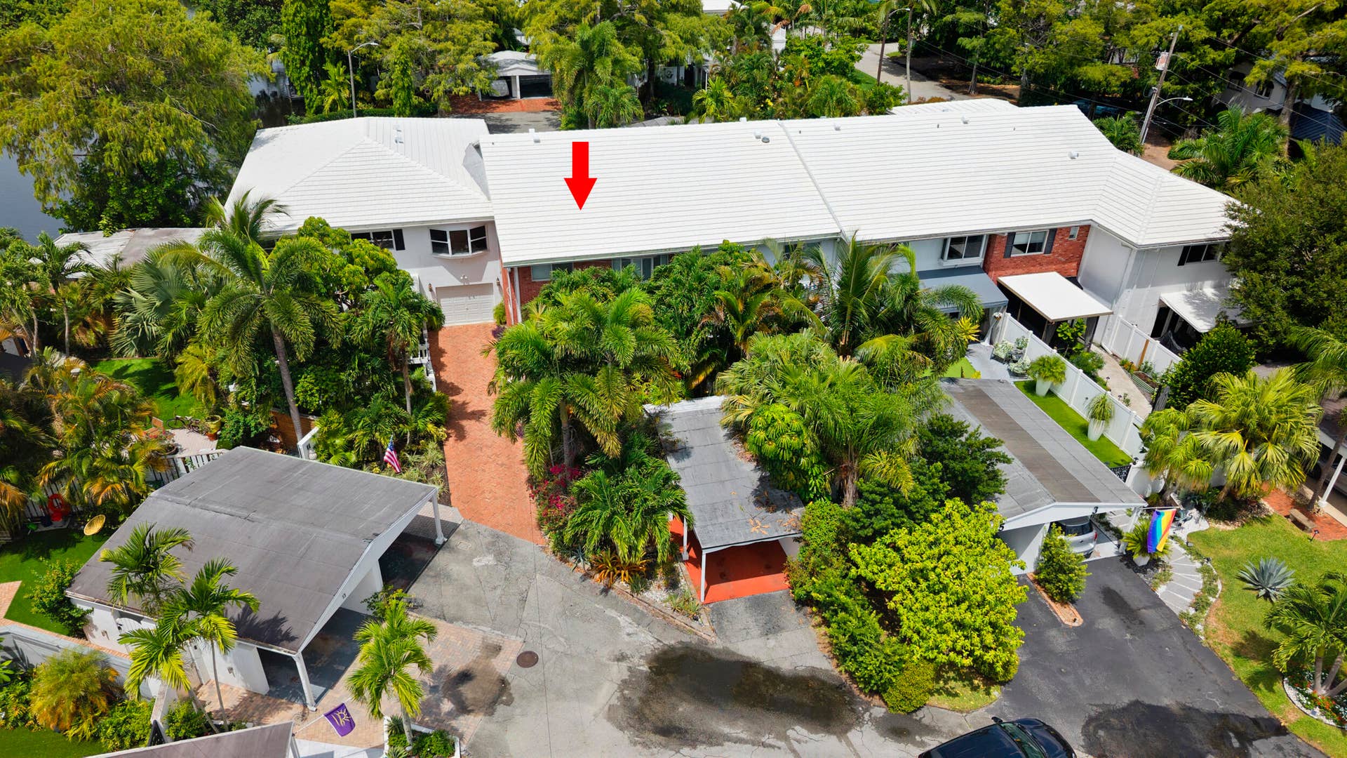 7 Middlesex Drive, Wilton Manors, FL 33305 Expansive mid-century modern residence with clean-lined white roof and brick entry court, surrounded by mature landscaping including palm trees and established greenery