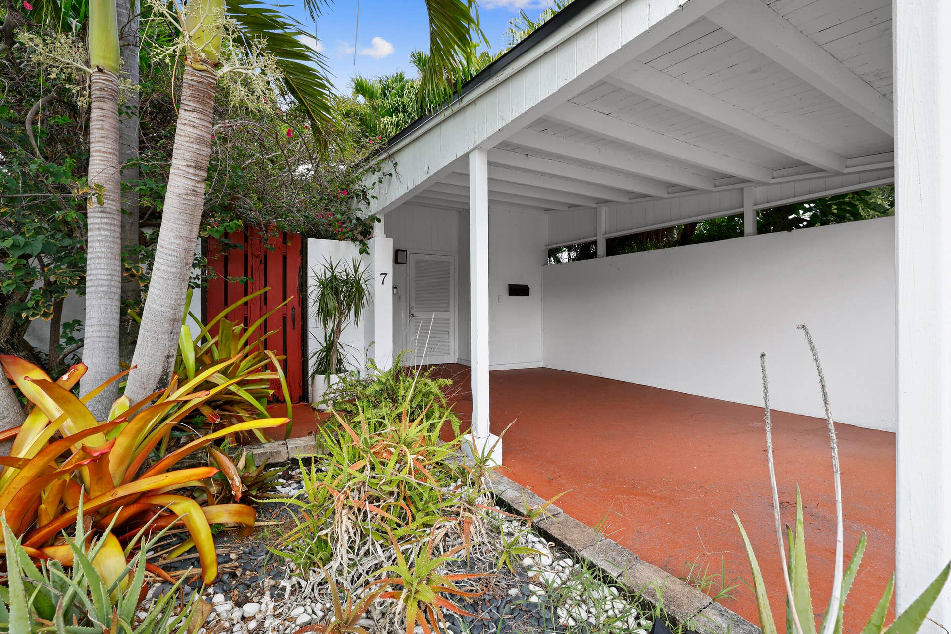 7 Middlesex Drive, Wilton Manors, FL 33305 Modern carport with polished concrete flooring in warm terracotta tones, featuring clean white structural beams and open-air design