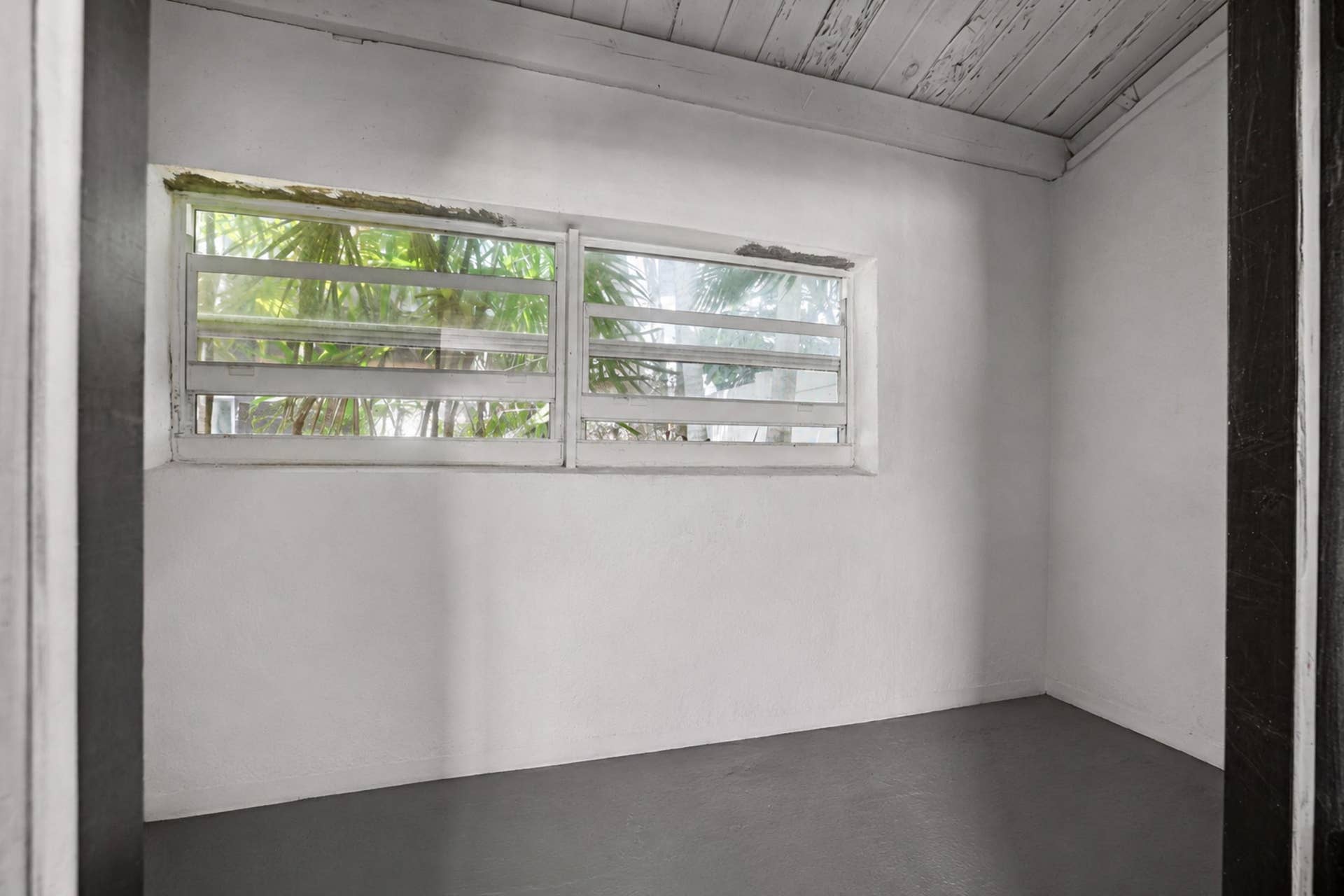 7 Middlesex Drive, Wilton Manors, FL 33305 Room featuring a wood-panel ceiling, window with exterior foliage, and dark gray flooring
