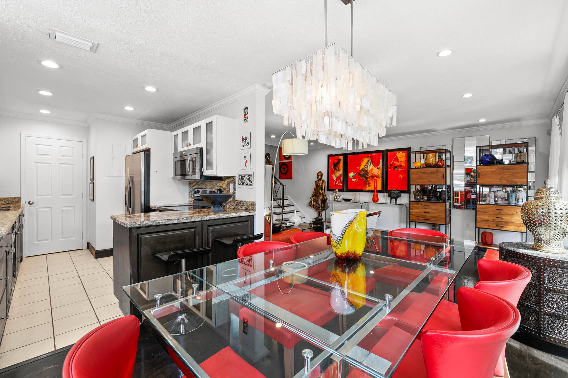 7 Middlesex Drive, Wilton Manors, FL 33305 Contemporary kitchen and dining area featuring a custom dark-finish island with waterfall countertop edge, stainless steel appliances, white cabinetry with integrated hardware, ceramic tile flooring, recessed and pendant lighting, and a dining table with seating for six