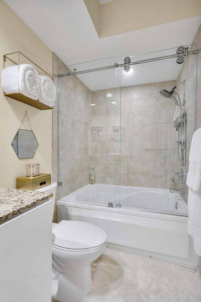 Bathroom featuring a spacious soaking tub with a glass sliding shower enclosure, a stone-finish countertop, tiled shower walls, and a recessed ceiling light