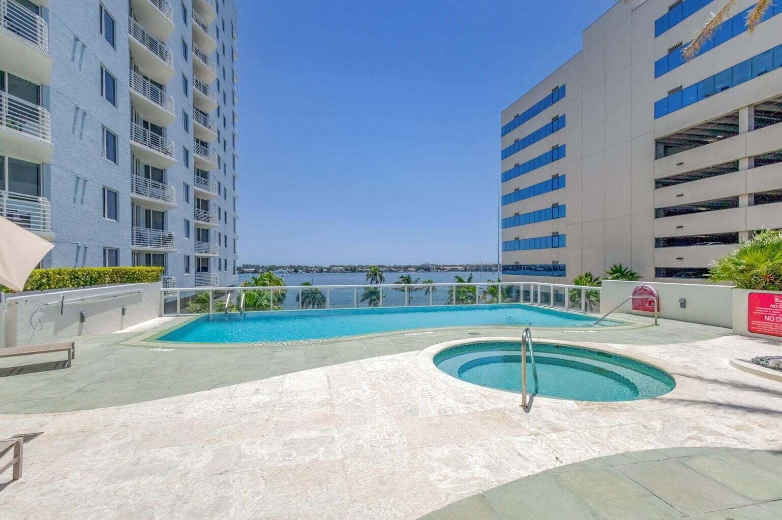 Resort-style pool deck featuring a swimming pool, integrated spa, and water backdrop