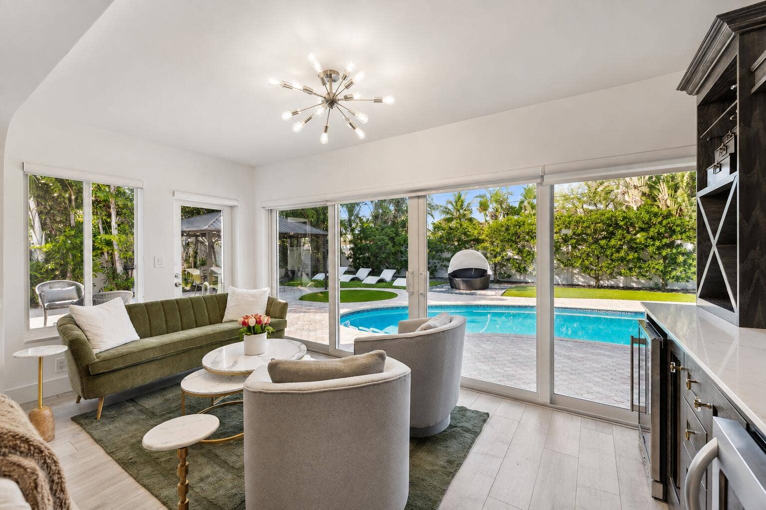 Sophisticated poolside living space featuring expansive sliding glass doors, light wood-finish flooring, and seamless indoor-outdoor connectivity