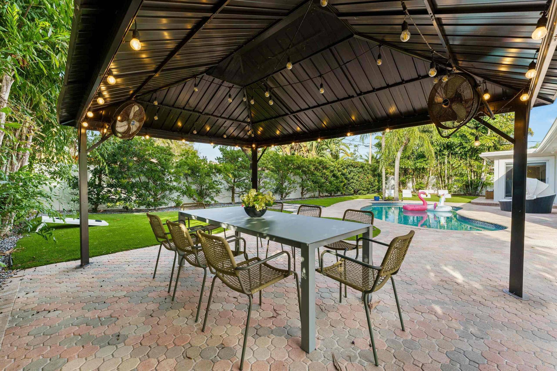 Sophisticated outdoor entertaining space featuring a sturdy metal pergola with integrated overhead lighting and ceiling fans, anchored by a spacious dining table with seating for six
