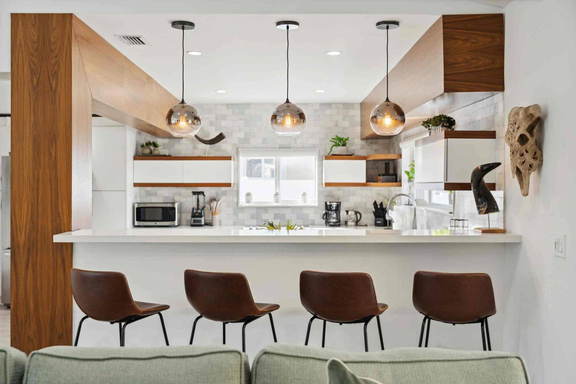 Kitchen featuring a white countertop island with integrated seating, three pendant lights, wood-finish beams, white cabinetry with wood-finish accents, and a tiled backsplash