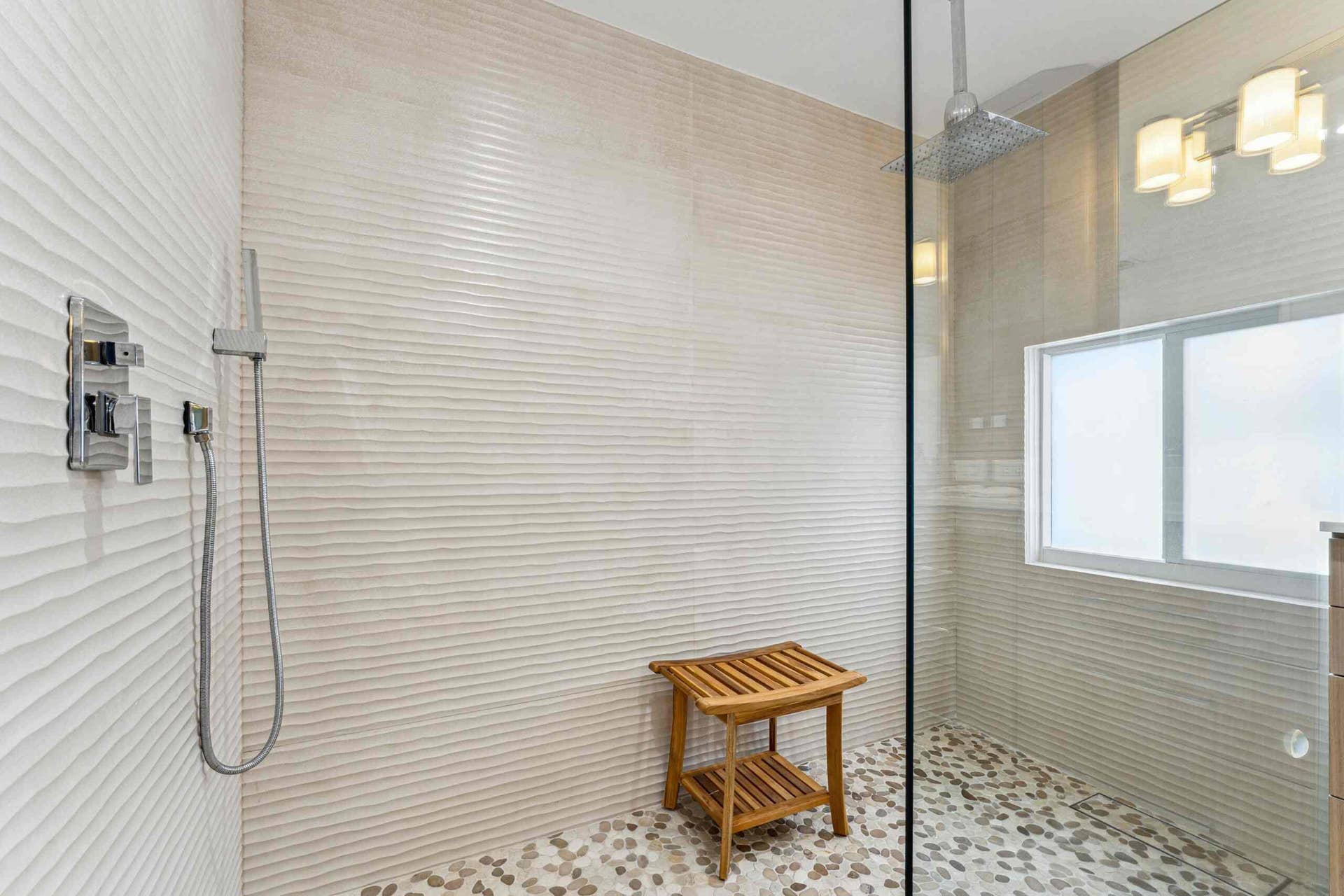 Walk-in shower featuring textured wall tiling, a rainfall showerhead, a hand-held shower fixture, and pebble-finish flooring