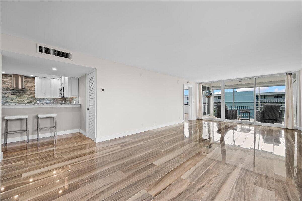 911 Ocean Drive, #601, Juno Beach, FL 33408 Open-concept living area featuring wood-finish flooring, a kitchen with light cabinetry, and a full-height glass sliding door opening to an outdoor balcony