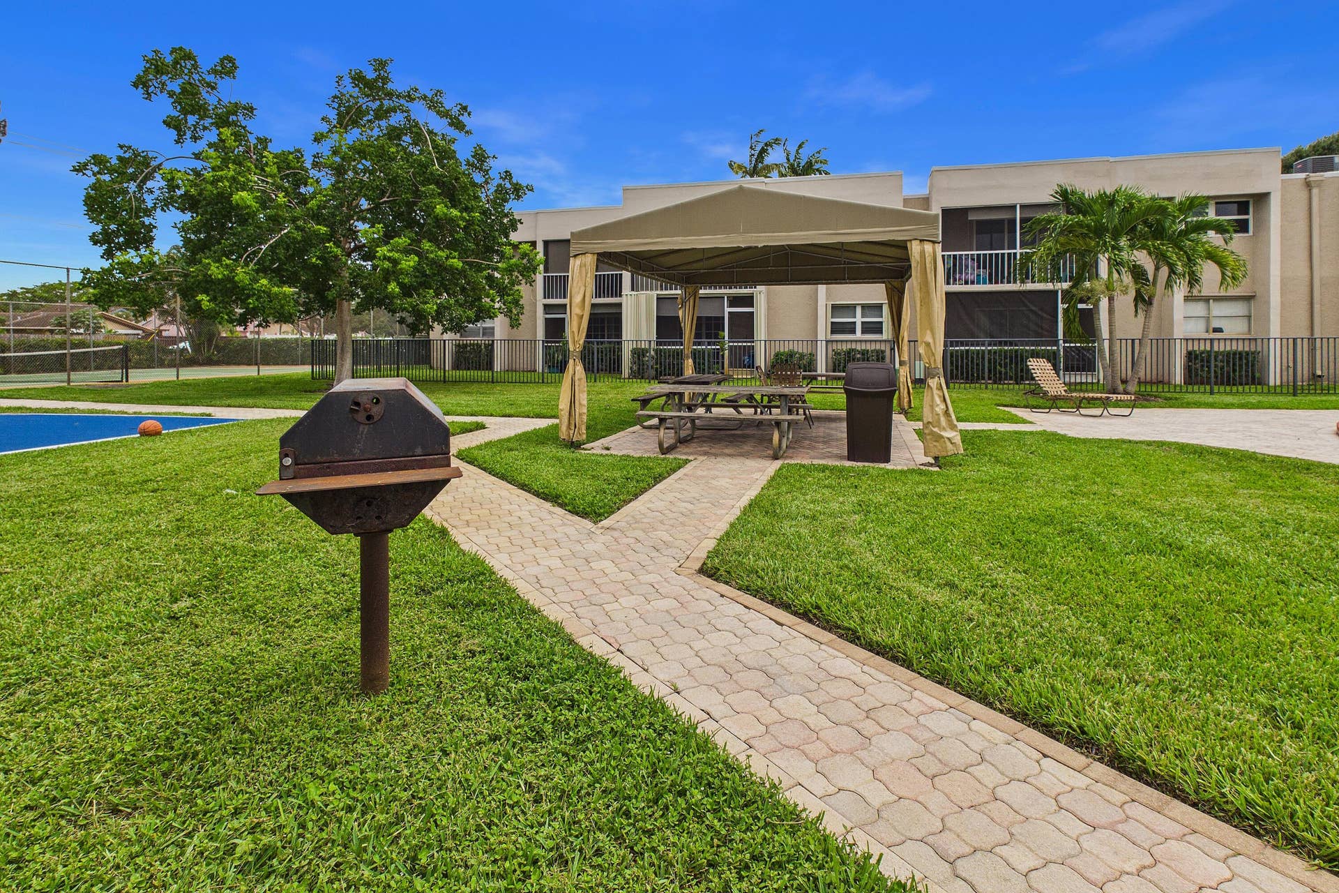 Expansive green space featuring a paved pathway, covered outdoor seating area, and a barbecue grill
