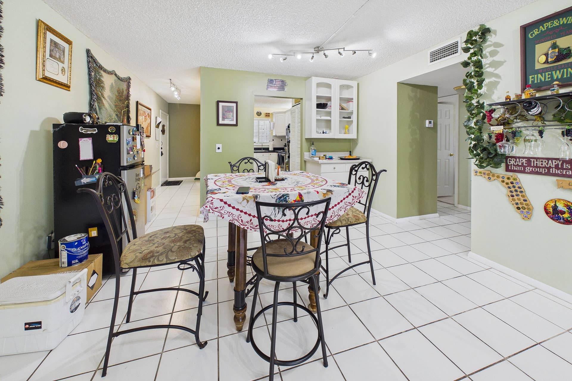 White tile flooring throughout, track lighting, and a partial kitchen with white cabinetry