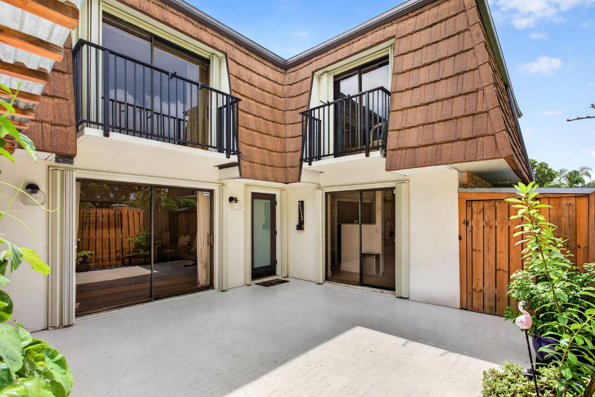 9113 SW 20th Court, #A, Davie, FL 33324 Private exterior patio with a light concrete finish, two upper-level balconies with black metal railings, and dual sliding glass doors
