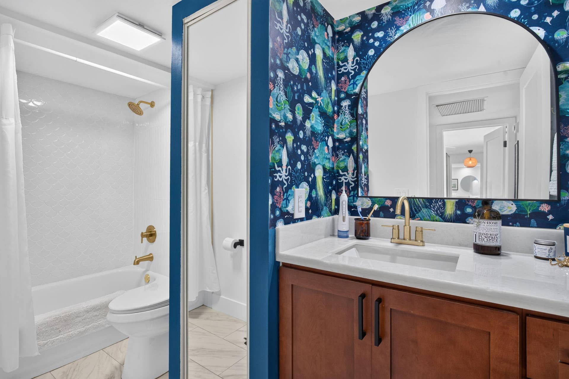 9113 SW 20th Court, #A, Davie, FL 33324 Bathroom featuring a vanity with wood-finish cabinetry, a white countertop with an integrated sink, an arched mirror, and a tub with an integrated shower