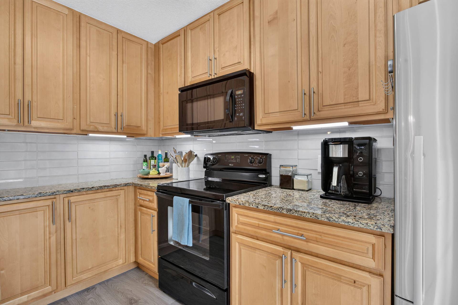 9113 SW 20th Court, #A, Davie, FL 33324 Wood-finish cabinetry, light-toned countertops, white subway tile backsplash, built-in microwave, and wood-finish flooring
