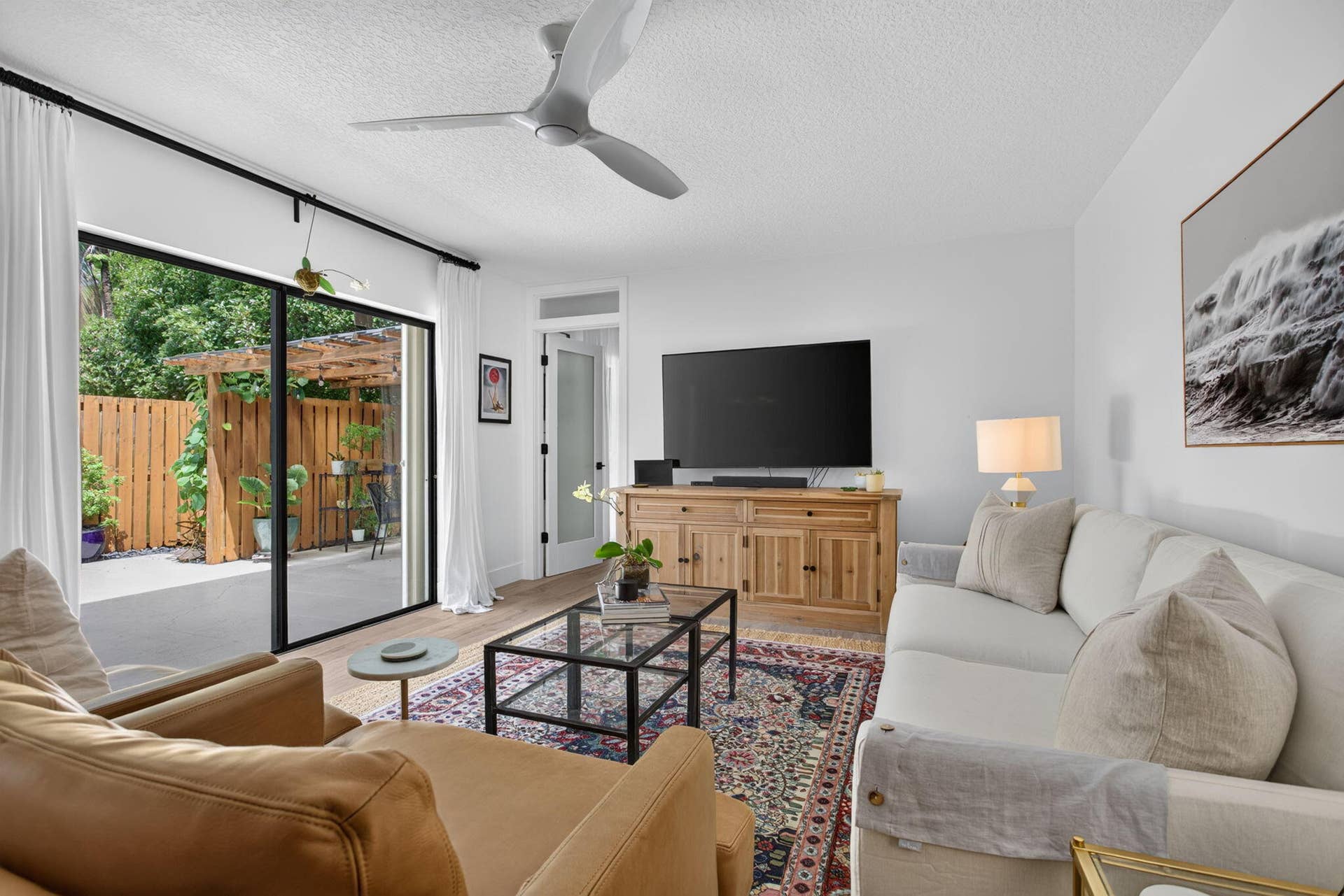 9113 SW 20th Court, #A, Davie, FL 33324 Sliding glass doors opening to an outdoor patio with a wooden privacy fence, wood-finish flooring, and a ceiling fan