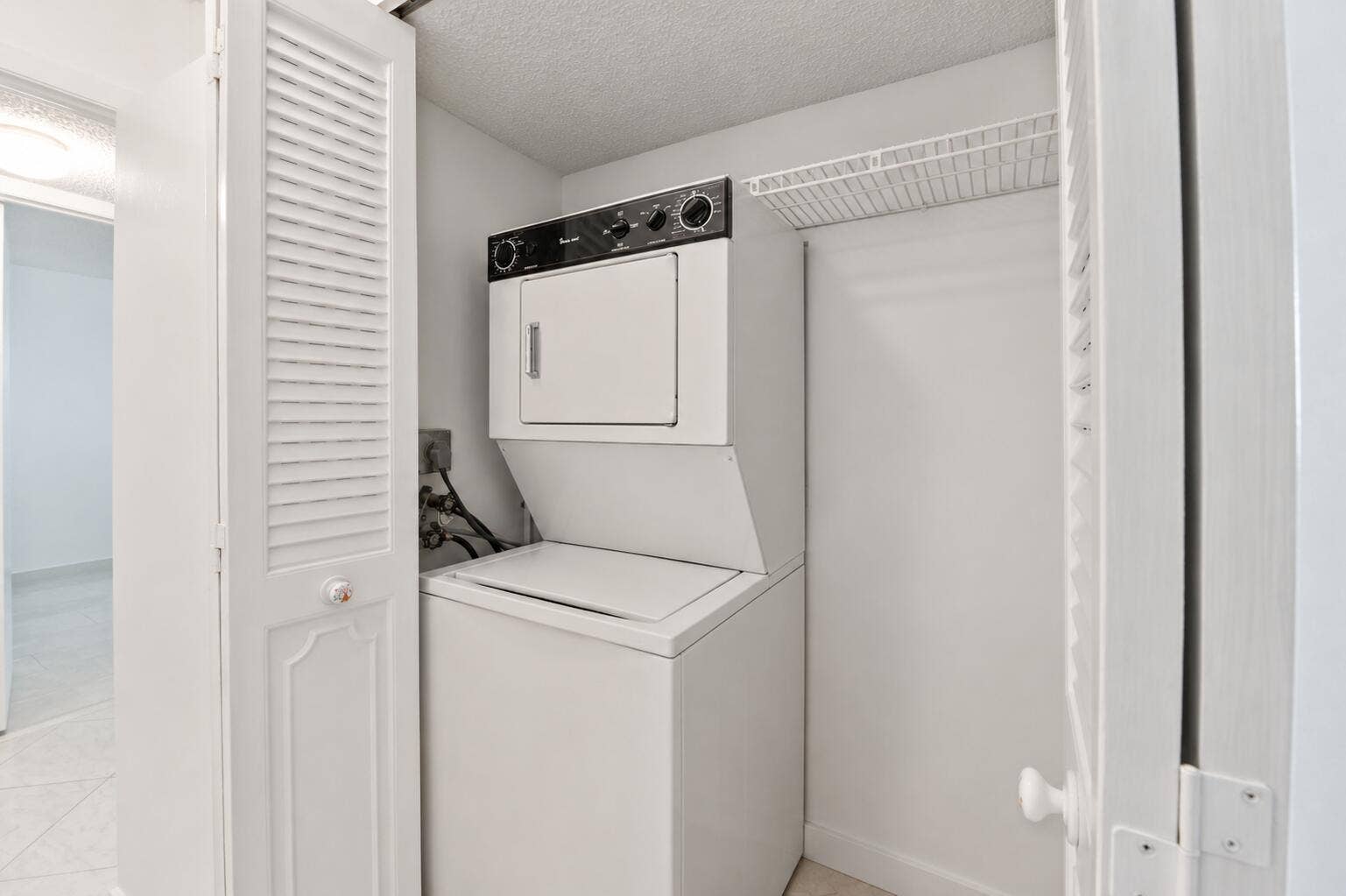 Integrated laundry closet with a stacked washer and dryer, louvered bi-fold doors, and shelving