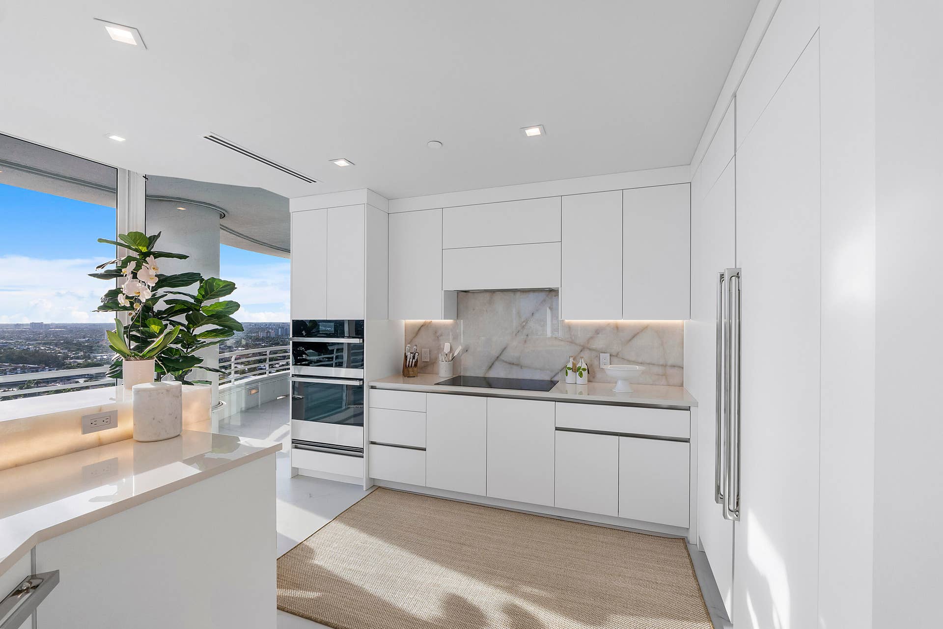 1700 S OCEAN Boulevard, #PH B-D, Lauderdale By The Sea, FL 33062 This magnificent chef's kitchen is a masterpiece of contemporary design, where luminous high-gloss white cabinetry is beautifully complemented by bespoke White Oak millwork and elegant glossy quartz countertops. At its heart, a breathtaking backlit Cristello natural stone island radiates a warm golden glow beneath matching Cristello backsplash & designer pendant chandeliers, creating a spectacular centerpiece for culinary artistry and sophisticated entertaining. Every detail has been thoughtfully curated to blend timeless elegance with exceptional functionality against a backdrop of panoramic ocean and city views.