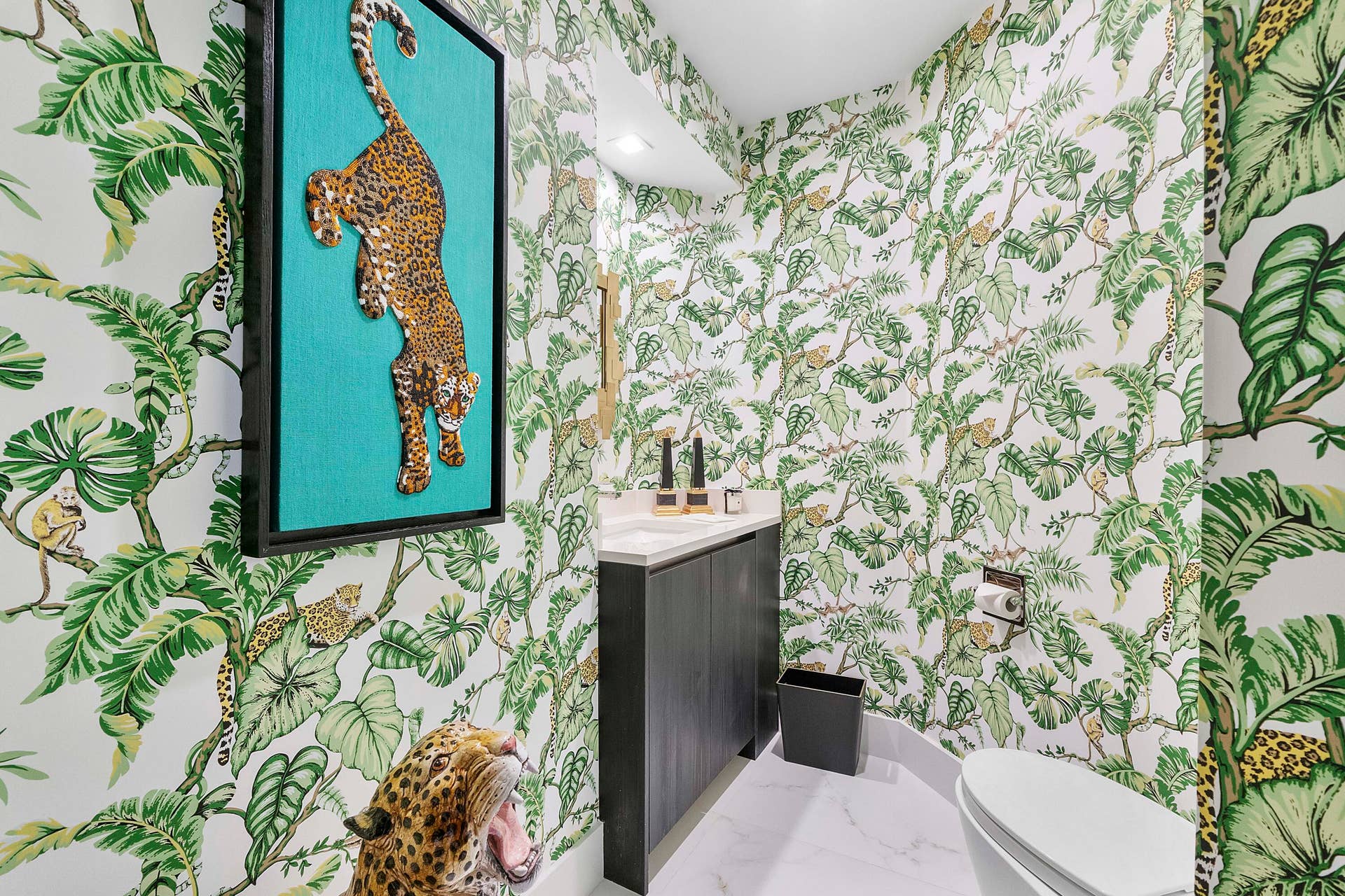 1700 S OCEAN Boulevard, #PH B-D, Lauderdale By The Sea, FL 33062 A hidden jewel at the end of the tropical hallway, this exceptionally private powder room is a delightful departure from the expected. Dramatic custom jungle-inspired wall coverings envelop the room, creating an immersive tropical setting filled with lush foliage and exotic leopards. The striking three-dimensional leopard artwork adds a playful couture-like touch, while the sleek contemporary vanity, crisp stone surfaces and refined fixtures balance the exuberant design. Intimate, unexpected and completely unique, this jewel-box powder room transforms an everyday space into an unforgettable designer experience for guests.