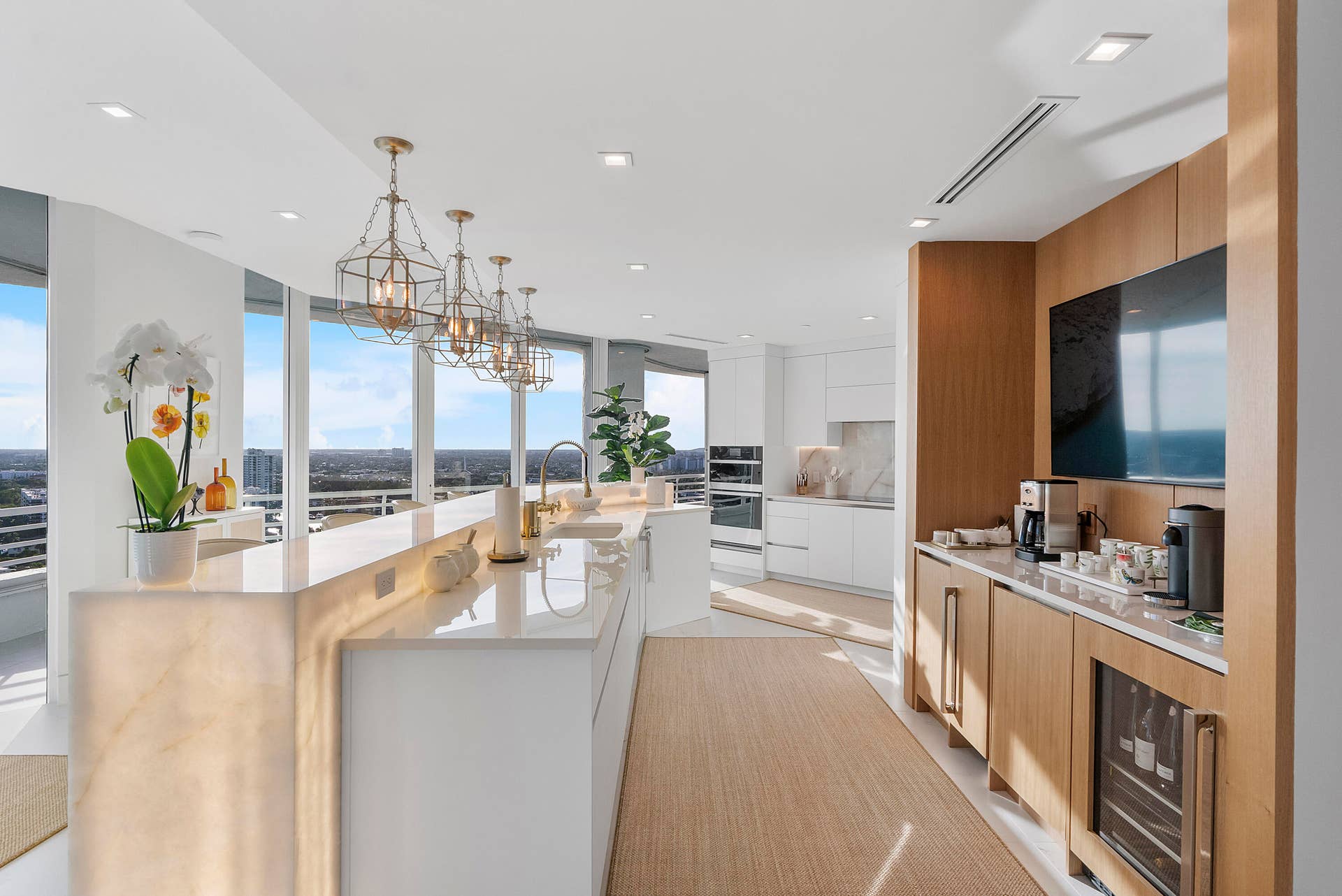 1700 S OCEAN Boulevard, #PH B-D, Lauderdale By The Sea, FL 33062 The spectacular chef's kitchen is a true showpiece, centered around a breathtaking backlit Cristallo natural stone island and countertops that radiate a warm golden glow, beautifully echoed by the custom pendant chandeliers suspended above. Designed for both everyday living and grand entertaining, this extraordinary culinary space blends exceptional craftsmanship with timeless elegance, while floor-to-ceiling glass and panoramic ocean views create an inspiring backdrop for every occasion.