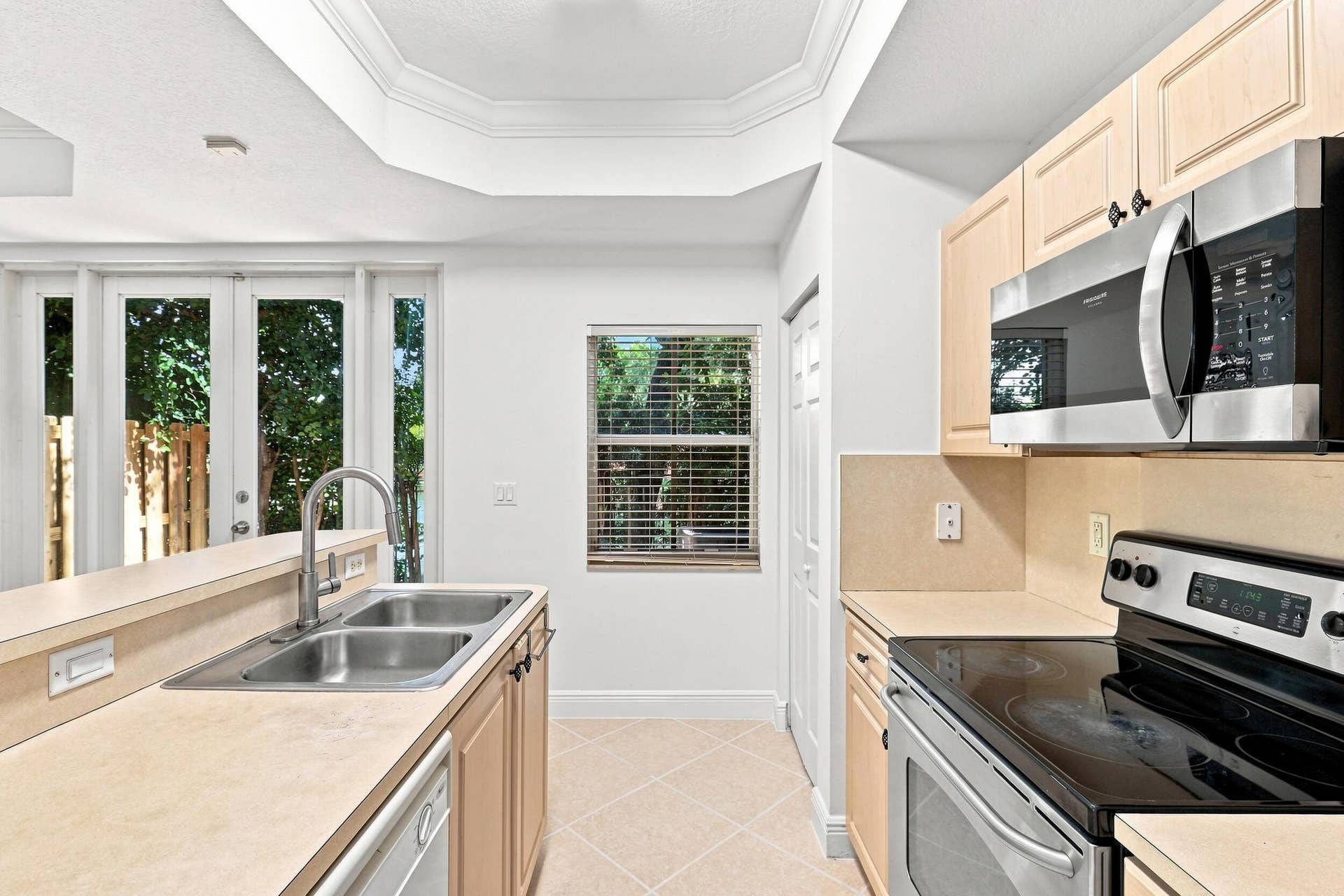 2107 Anchor Court, Fort Lauderdale, FL 33312 Bright, functional kitchen featuring ample cabinetry, stainless steel appliances, a double-basin sink, breakfast bar seating, and distinctive tray ceiling details. The open design provides an easy connection to the adjoining living and dining areas.