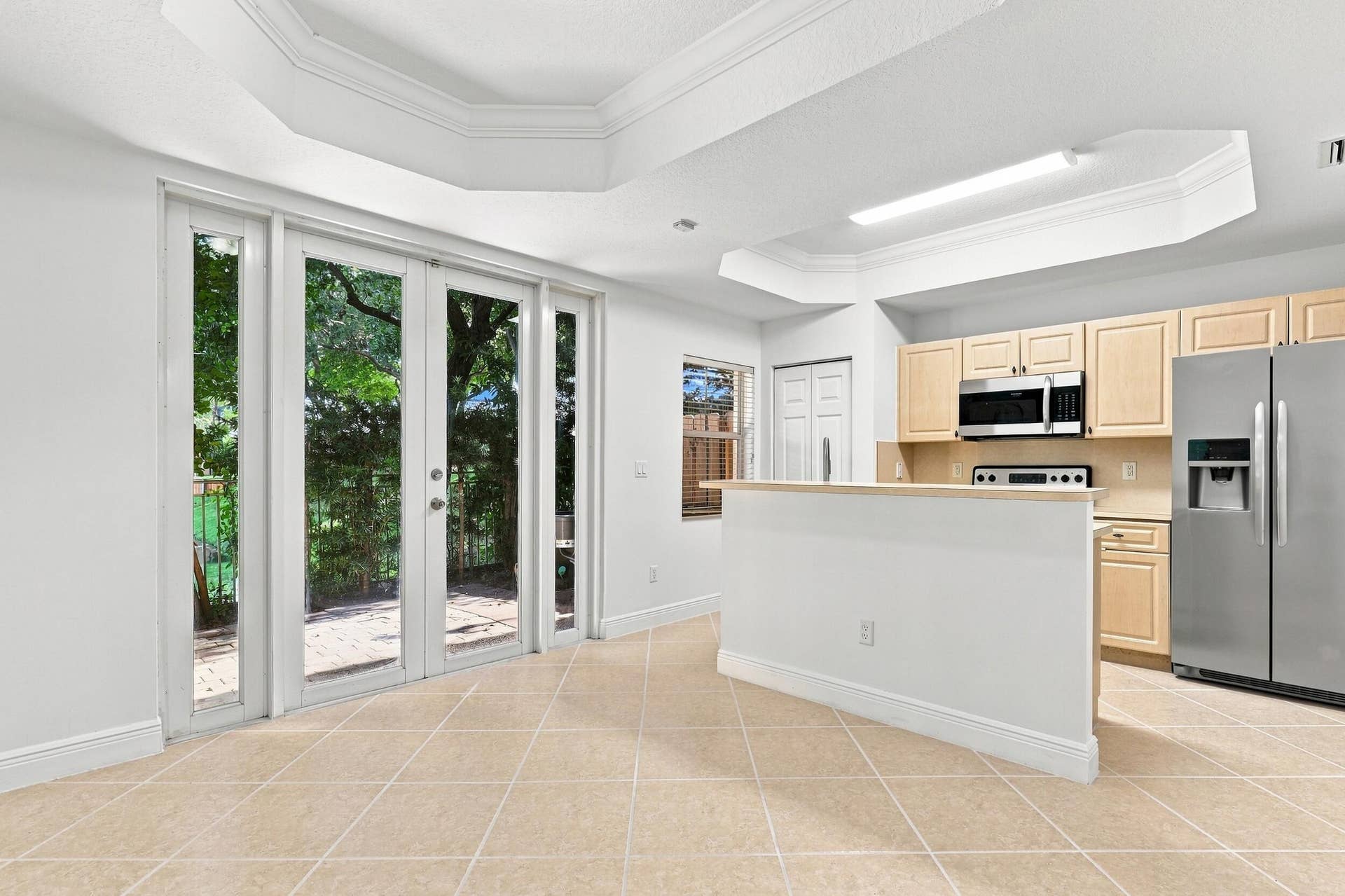 2107 Anchor Court, Fort Lauderdale, FL 33312 Bright dining area featuring tile flooring, a decorative tray ceiling with crown molding, and French doors that bring in natural light and provide direct access to the private outdoor patio. The open layout connects seamlessly with the kitchen for easy everyday living and entertaining.