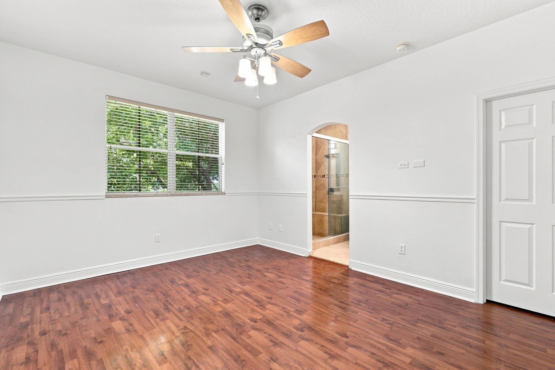 2107 Anchor Court, Fort Lauderdale, FL 33312 Spacious primary suite featuring warm wood flooring, abundant natural light, a large window overlooking lush greenery, and direct access to the private ensuite bathroom. The generous layout provides plenty of space and creates a comfortable private retreat.