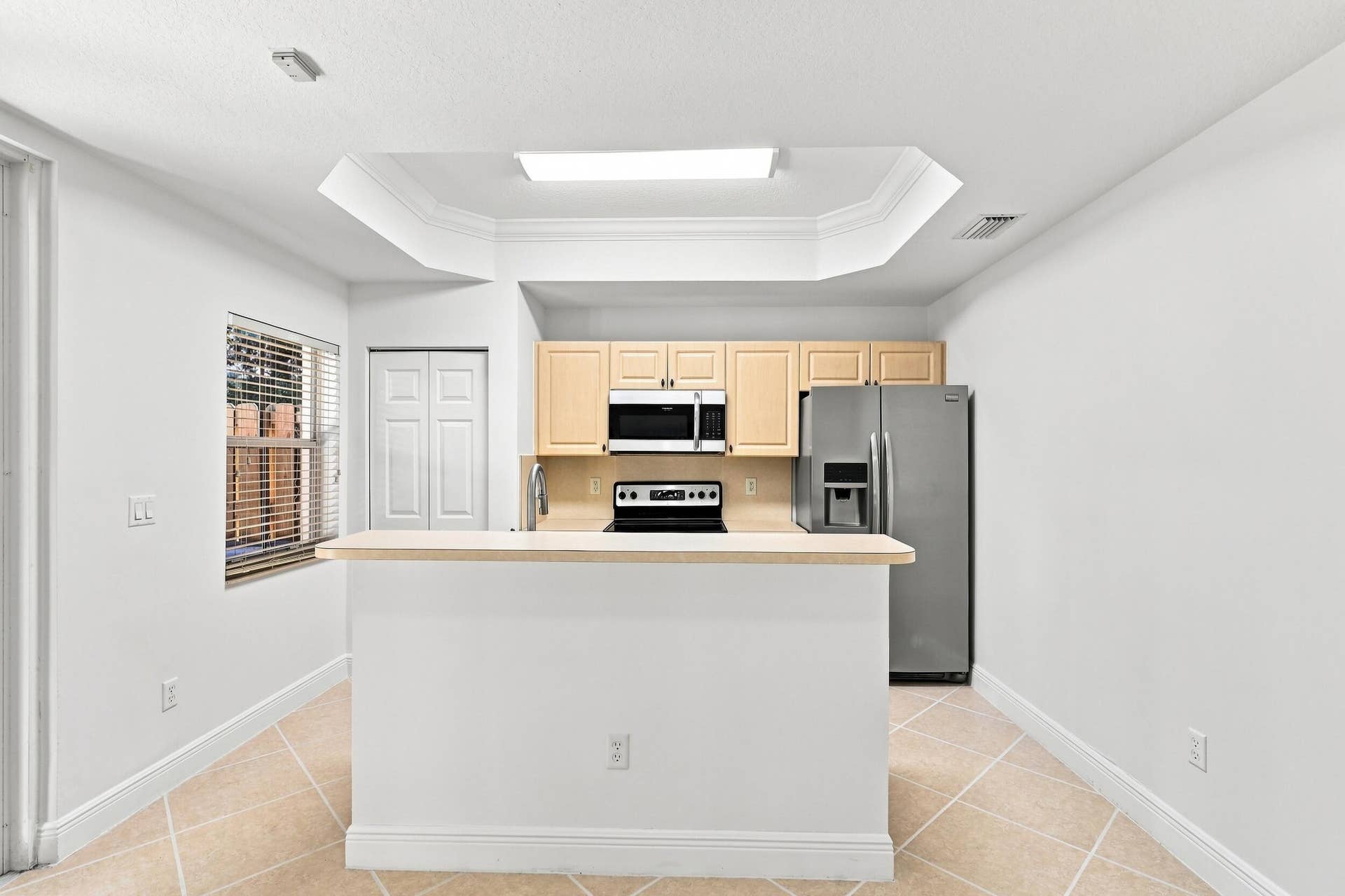 2107 Anchor Court, Fort Lauderdale, FL 33312 Bright, functional kitchen featuring ample cabinetry, stainless steel appliances, a double-basin sink, breakfast bar seating, and distinctive tray ceiling details. The open design provides an easy connection to the adjoining living and dining areas.