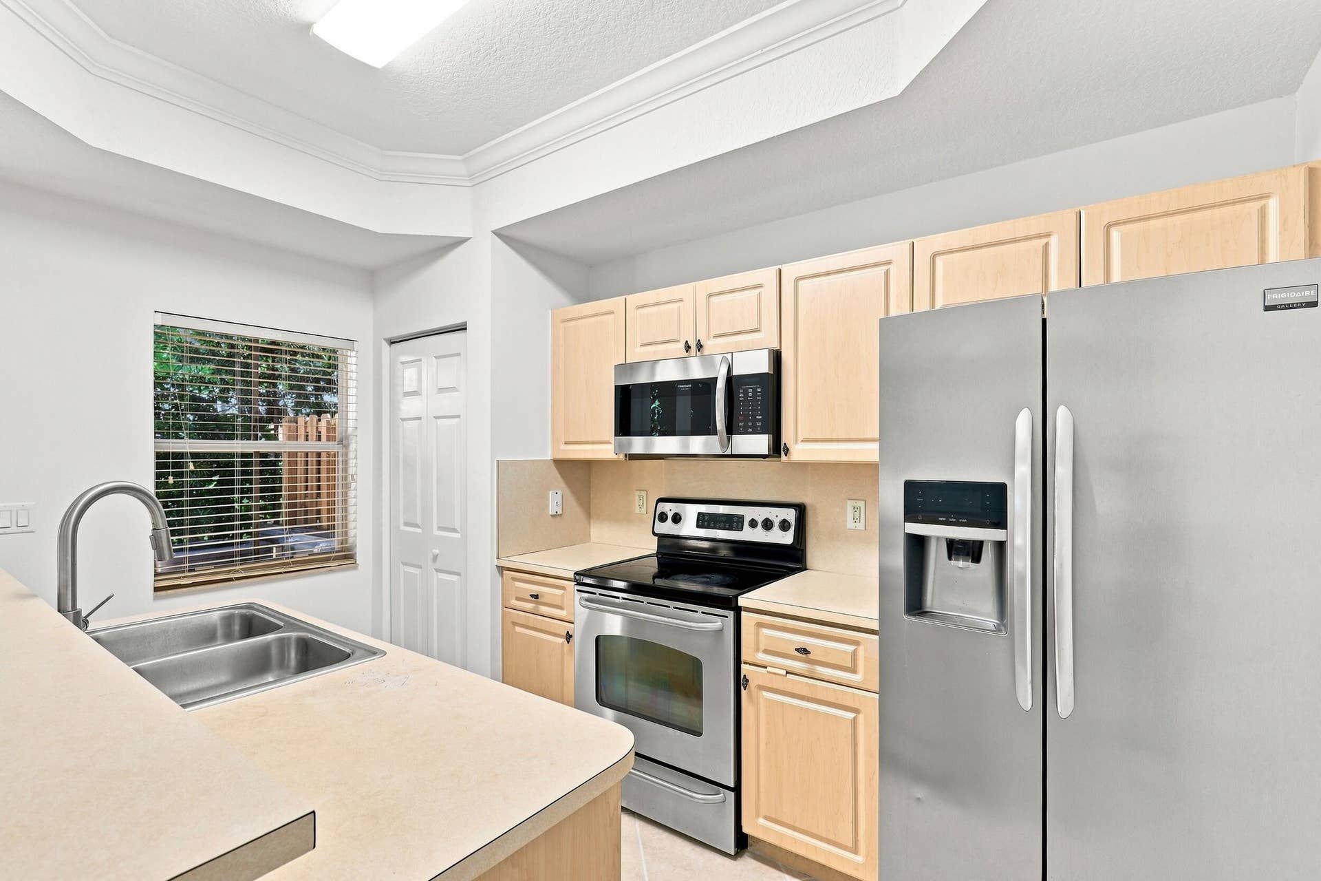 2107 Anchor Court, Fort Lauderdale, FL 33312 Bright, functional kitchen featuring ample cabinetry, stainless steel appliances, a double-basin sink, breakfast bar seating, and distinctive tray ceiling details. The open design provides an easy connection to the adjoining living and dining areas.