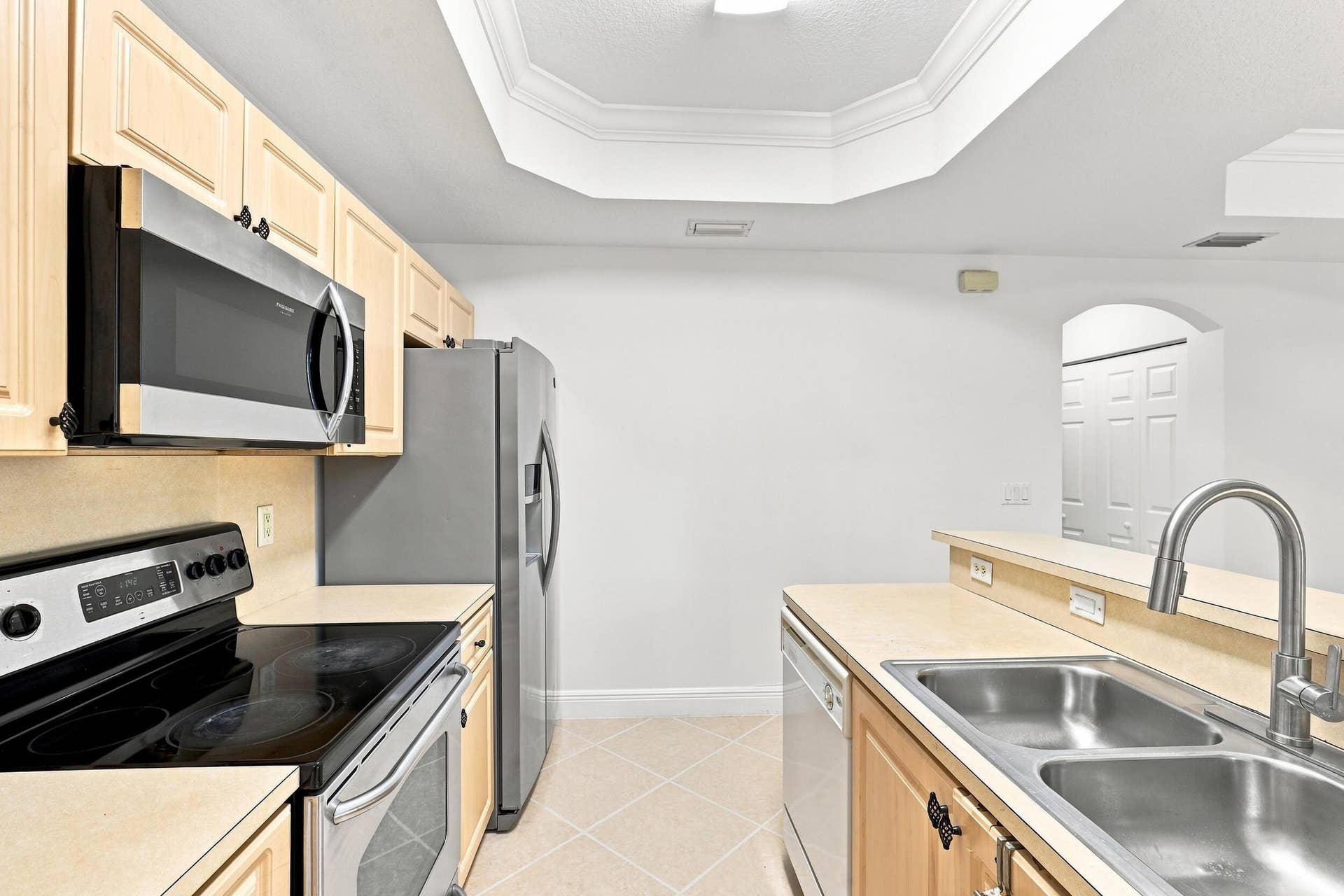 2107 Anchor Court, Fort Lauderdale, FL 33312 Bright, functional kitchen featuring ample cabinetry, stainless steel appliances, a double-basin sink, breakfast bar seating, and distinctive tray ceiling details. The open design provides an easy connection to the adjoining living and dining areas.
