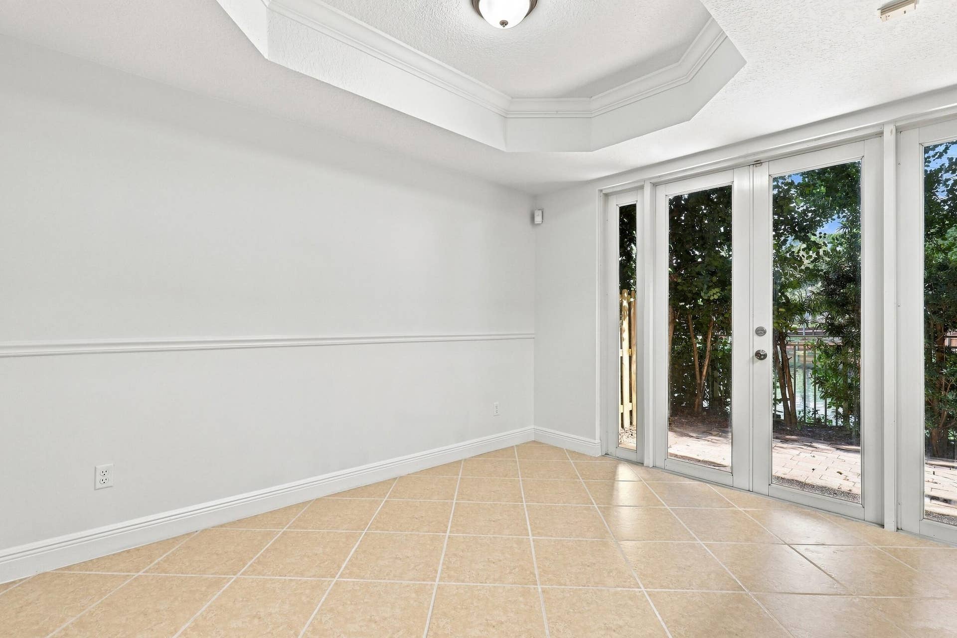 2107 Anchor Court, Fort Lauderdale, FL 33312 Bright dining area featuring tile flooring, a decorative tray ceiling with crown molding, and French doors that bring in natural light and provide direct access to the private outdoor patio. The open layout connects seamlessly with the kitchen for easy everyday living and entertaining.
