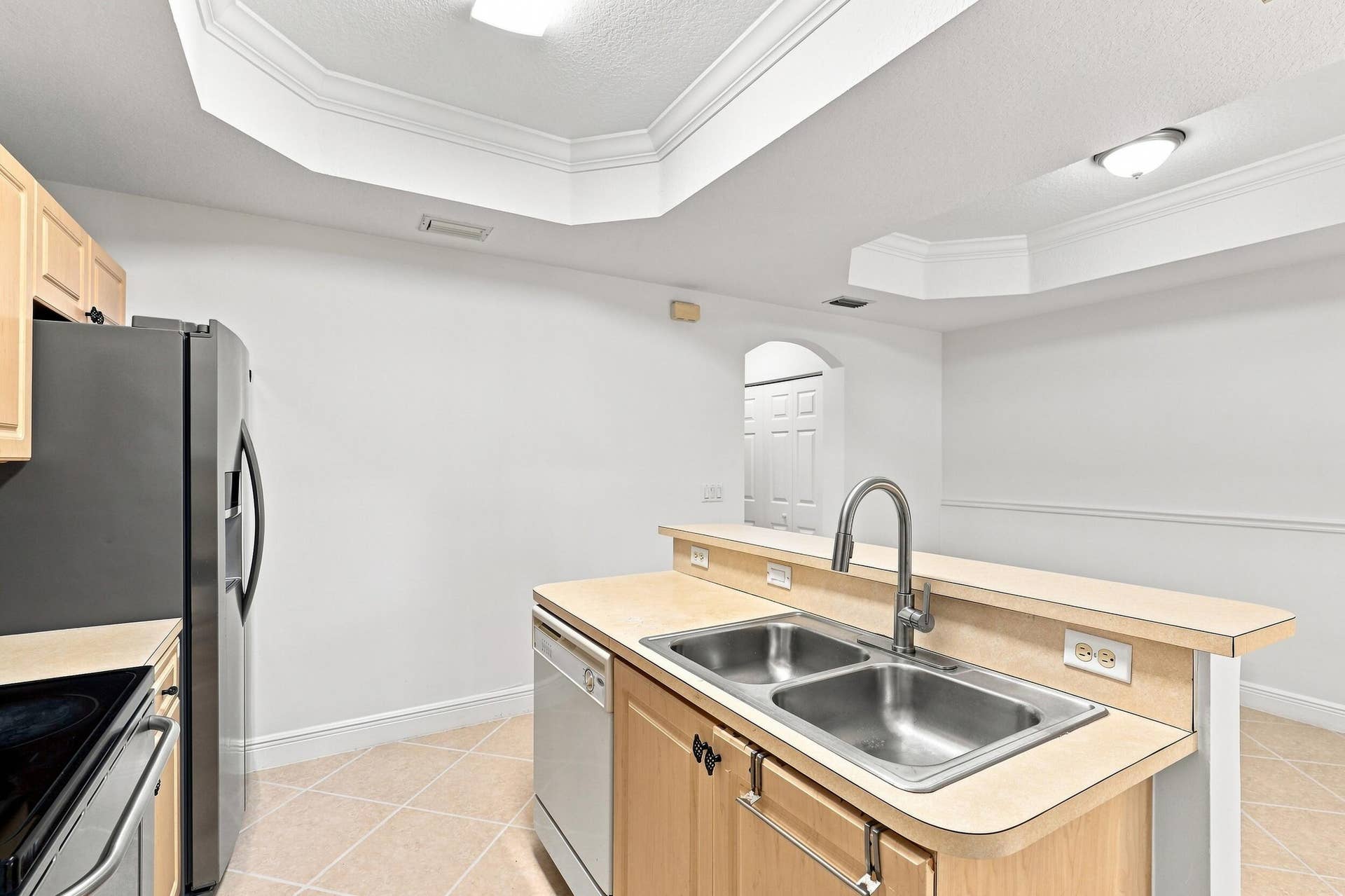 2107 Anchor Court, Fort Lauderdale, FL 33312 Bright, functional kitchen featuring ample cabinetry, stainless steel appliances, a double-basin sink, breakfast bar seating, and distinctive tray ceiling details. The open design provides an easy connection to the adjoining living and dining areas.